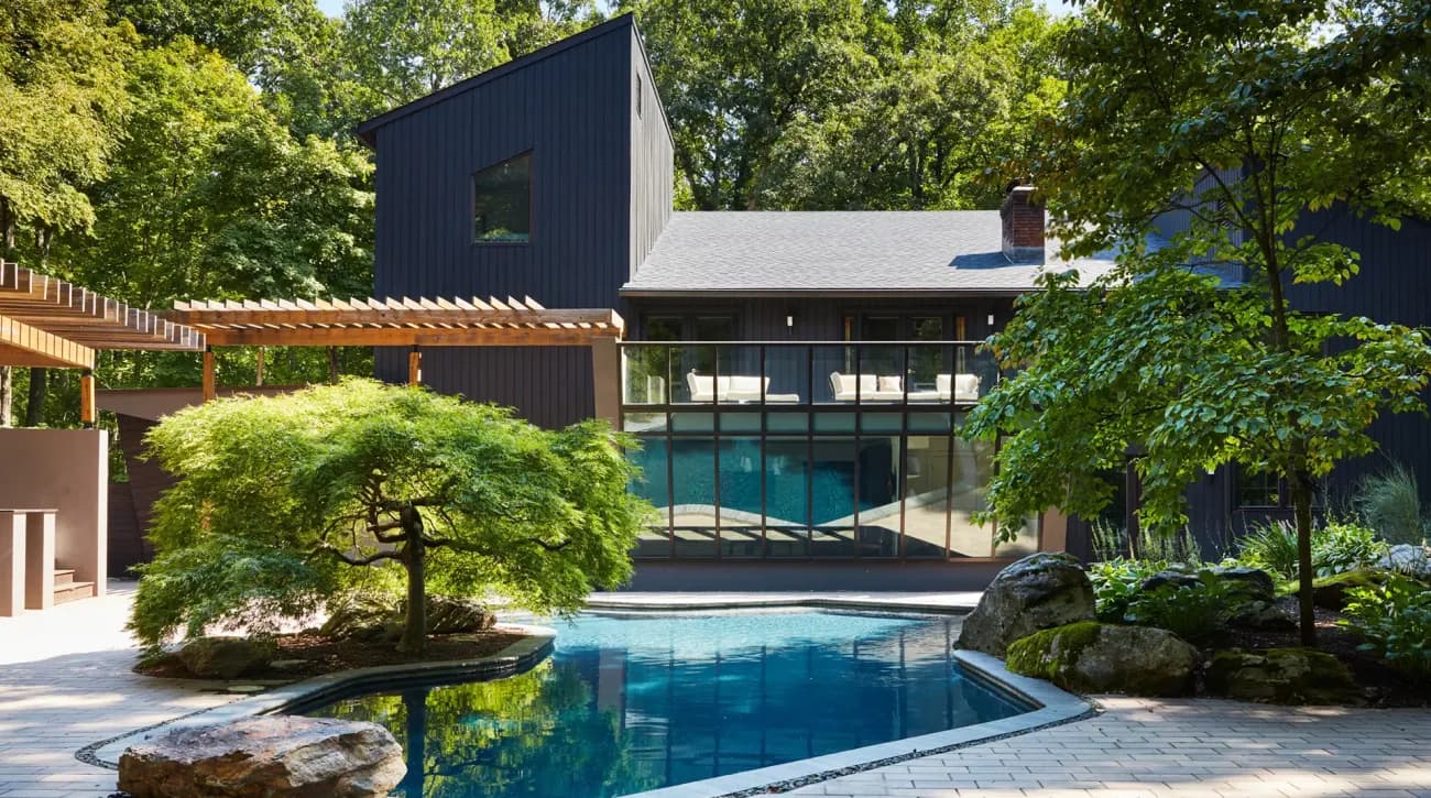 Contemporary residential courtyard with reflecting pool, dark metal and glass structures, lush landscaping, and modern architectural elements by Scott Springer Architect LLC.
