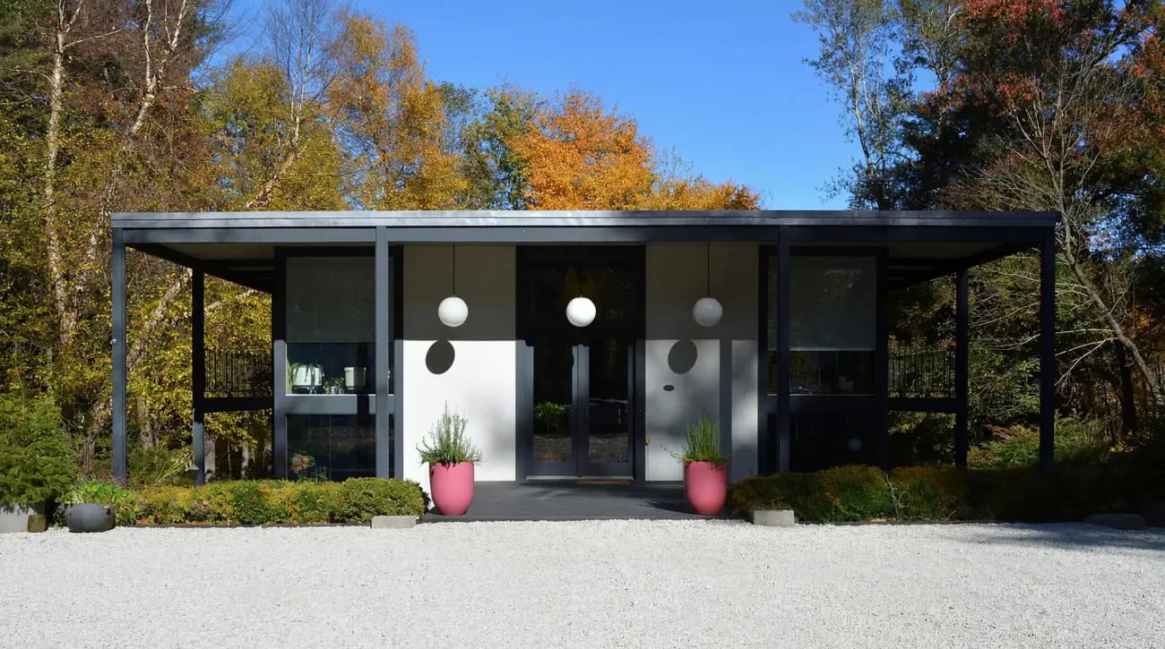 Modern black and glass pavilion with cantilevered roof and pink planters set among fall foliage, designed by Scott Springer Architect LLC.