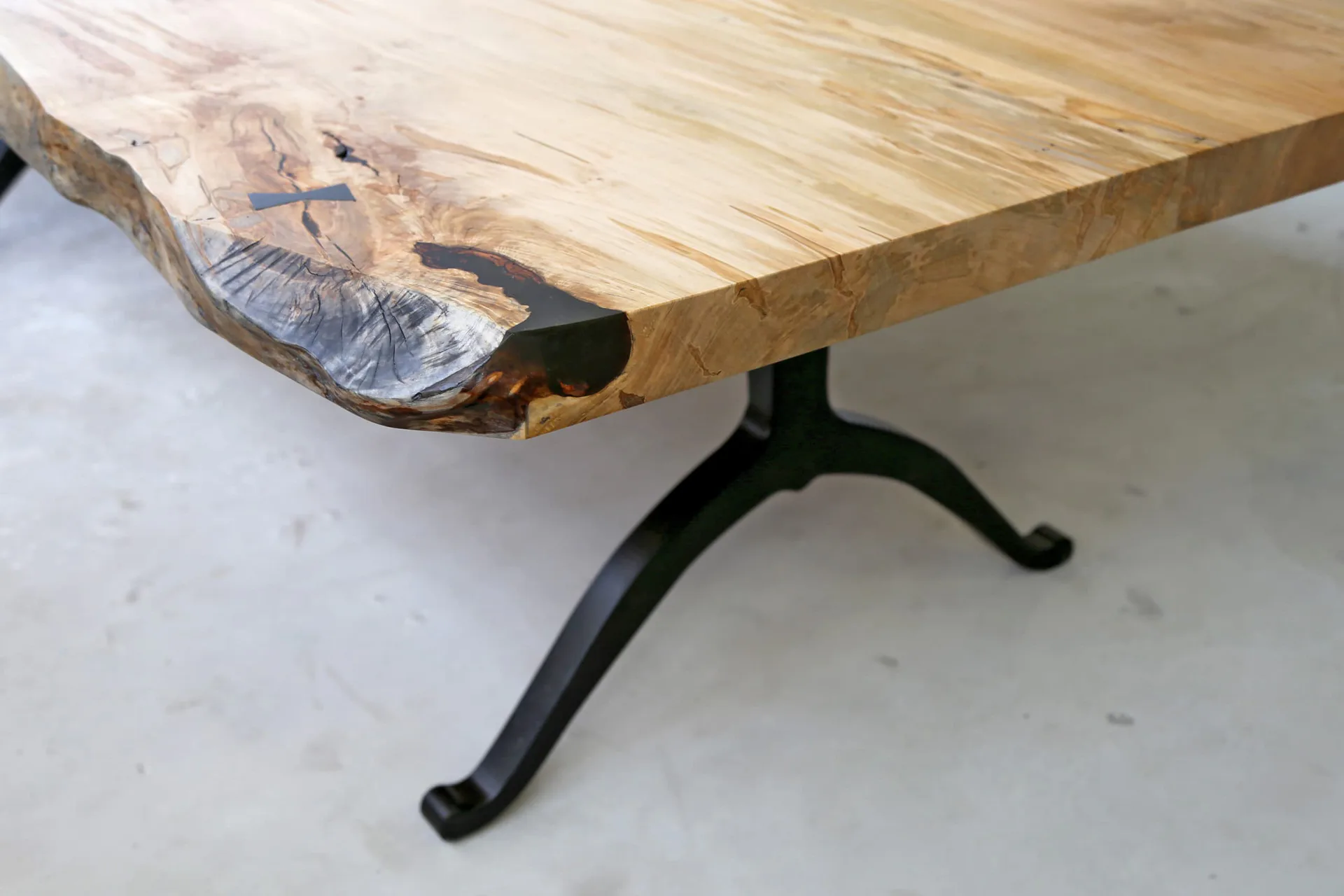 Live-edge wood table with natural grain patterns and dark cast-iron tripod base on neutral flooring, by SENTIENT.