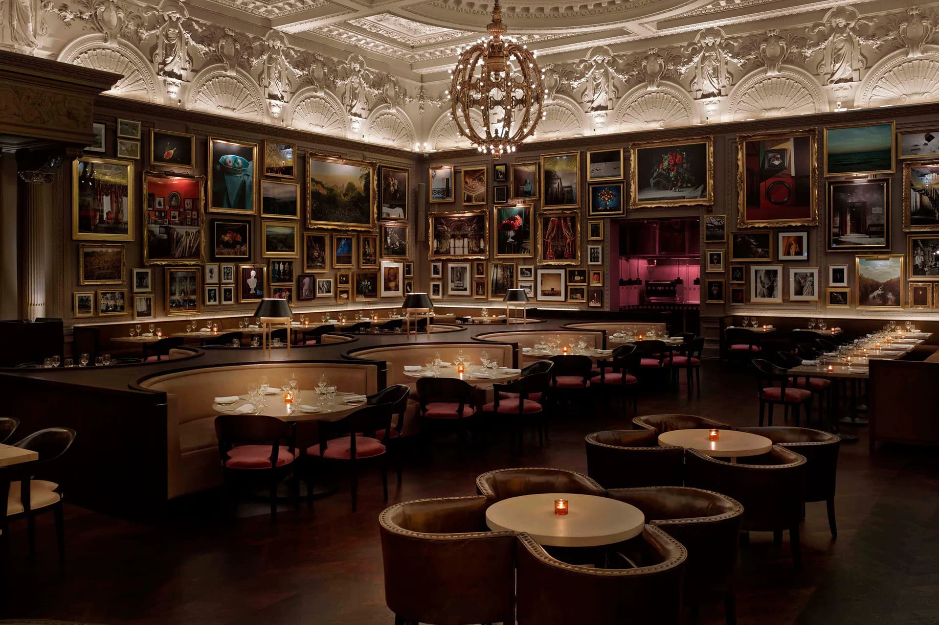 Elegant dining room with ornate ceiling, gallery walls displaying classical artwork, dark wood furnishings, candlelit round tables, and dramatic pendant lighting by SENTIENT.