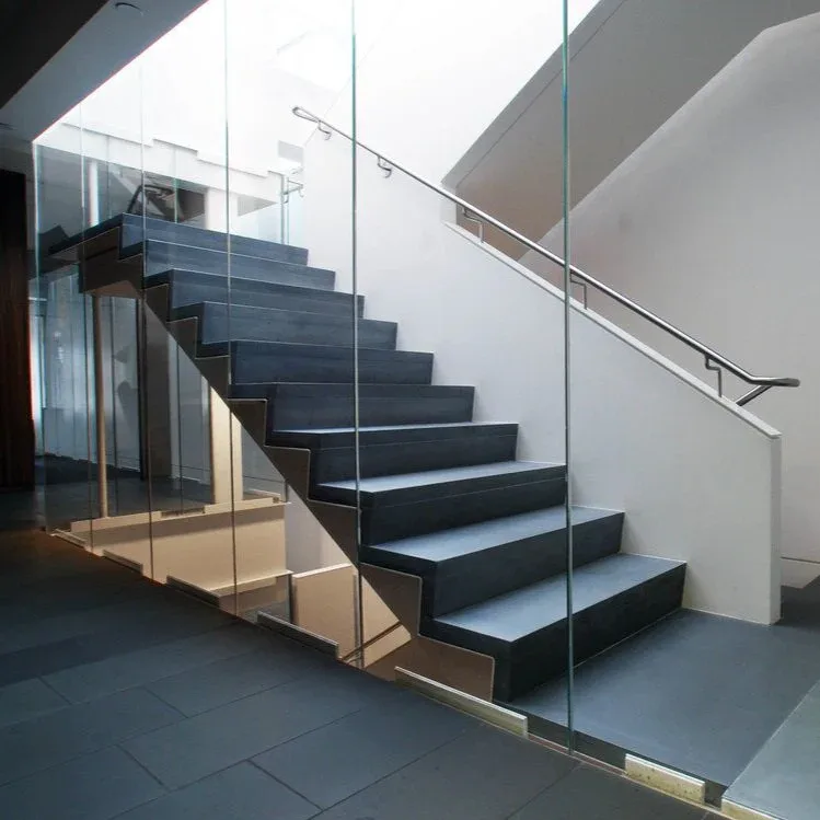Modern staircase with dark metal steps and glass railings in minimalist interior space by Serett Metalworks.