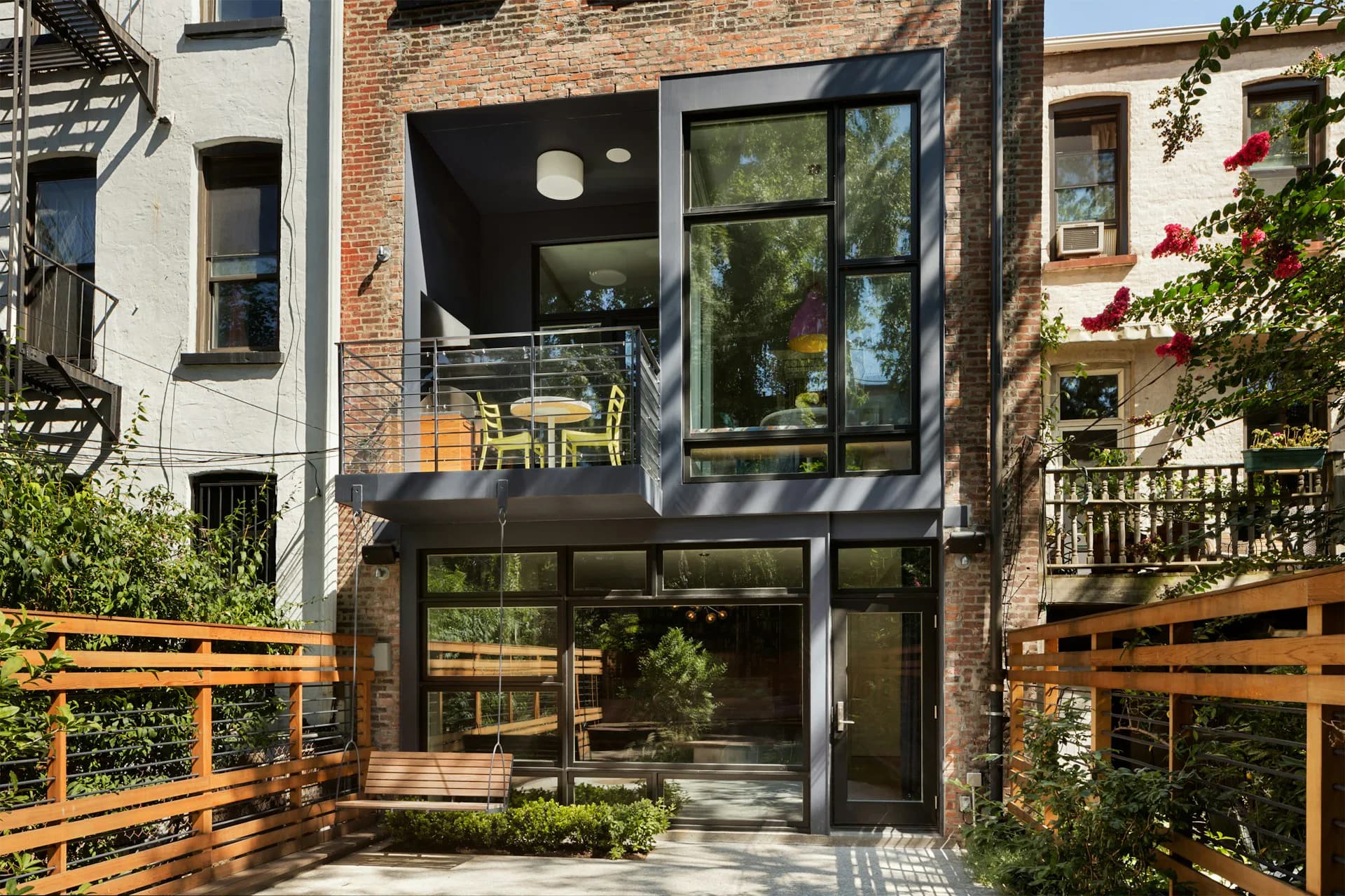 Modern brick townhouse exterior with black-framed glass storefront, wooden fence gates, and planted courtyard by Shakespeare Gordon Studio.