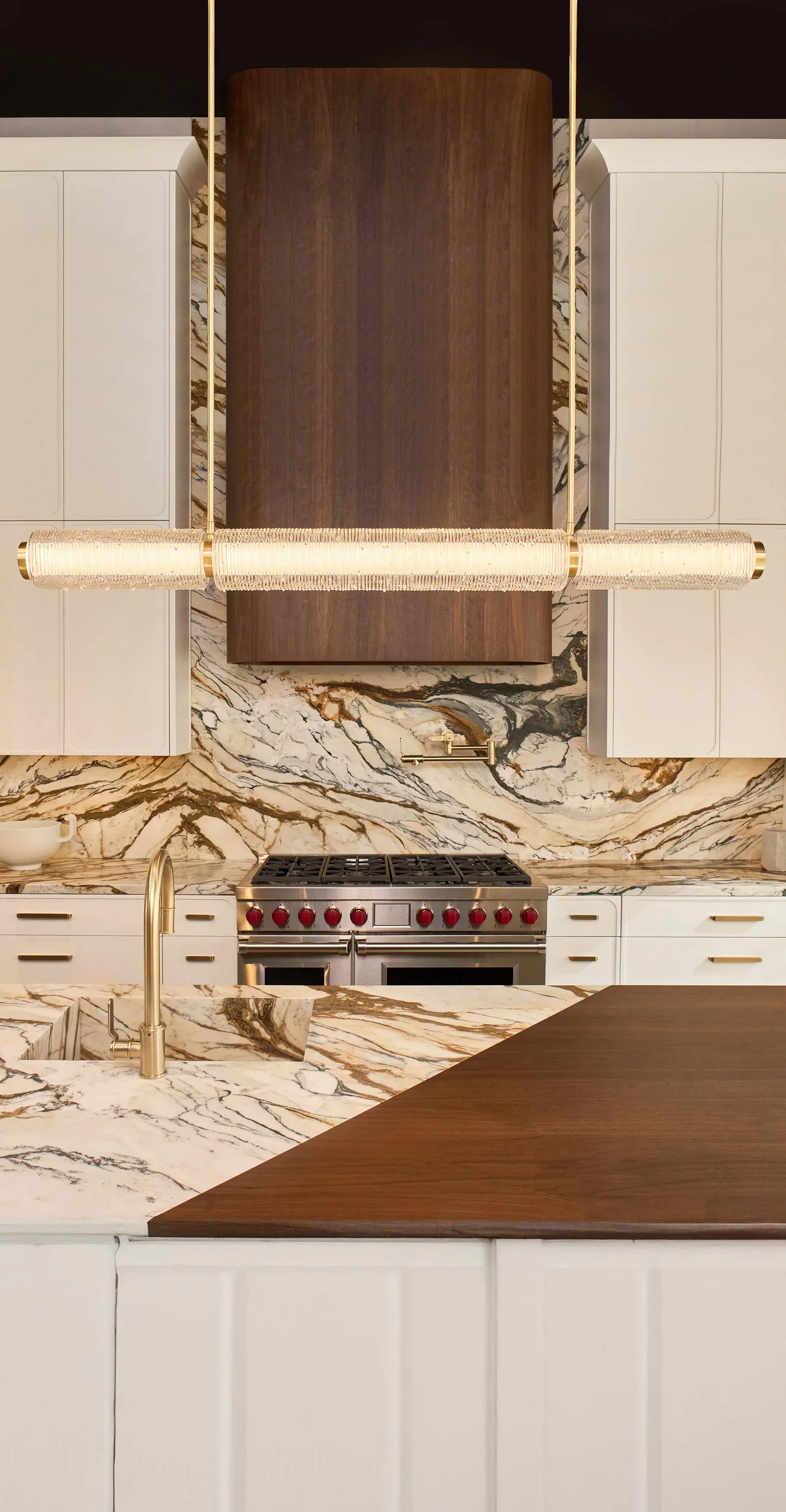 Luxurious kitchen with white cabinetry, marble backsplash and countertops, brass accents, and a dual-fuel range, designed by Shakúff.