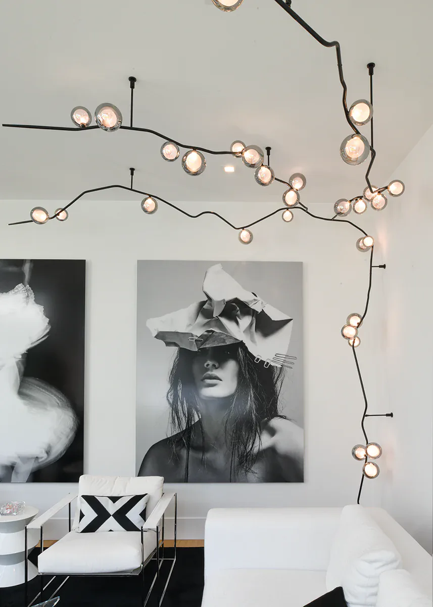 Modern bedroom interior with sculptural wire-and-sphere pendant lighting installation, black-and-white portrait photography on wall, and minimalist furnishings by Shakuff.