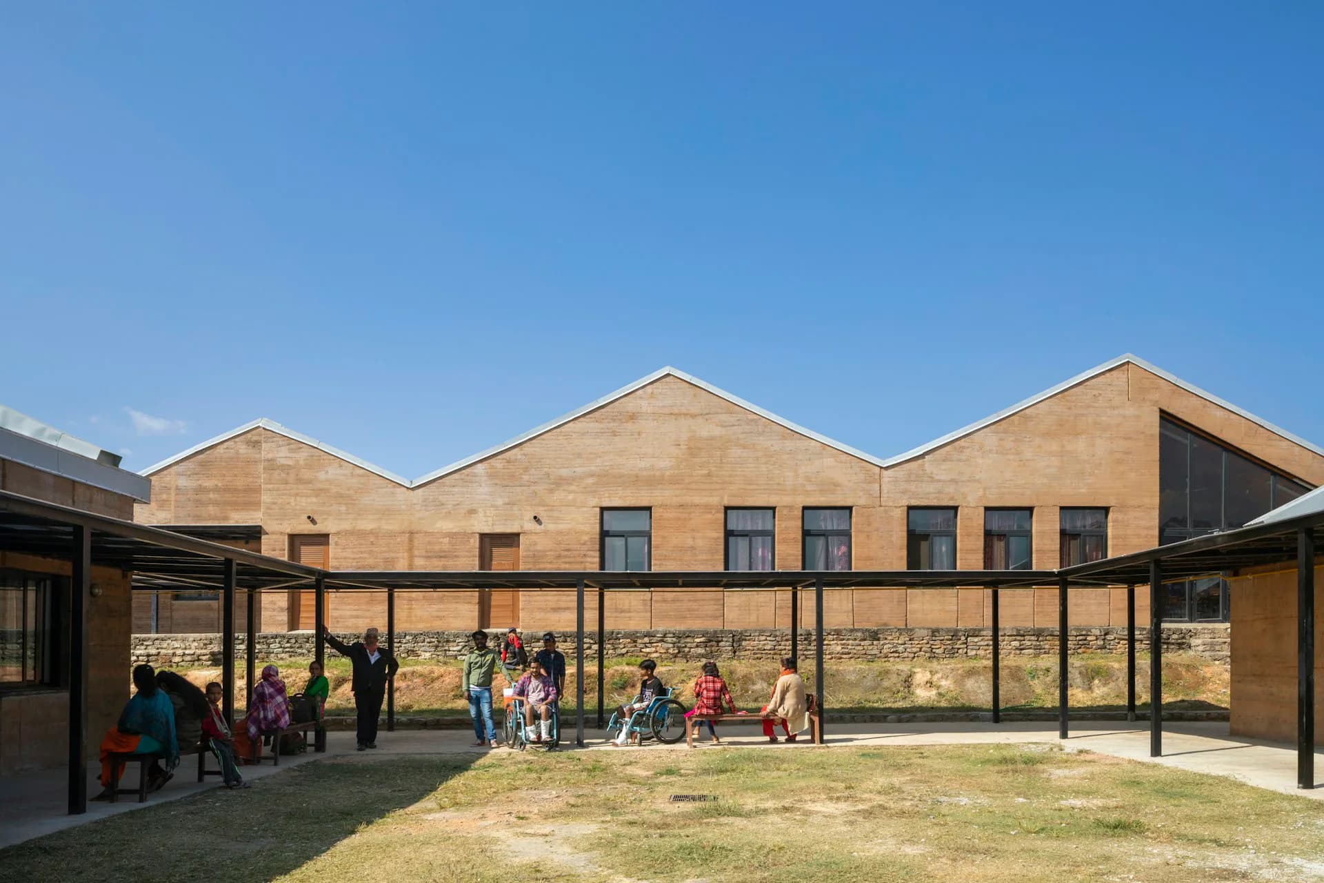 Brick school building with pitched roof and covered courtyard featuring children and staff, designed by Sharon Davis Design.