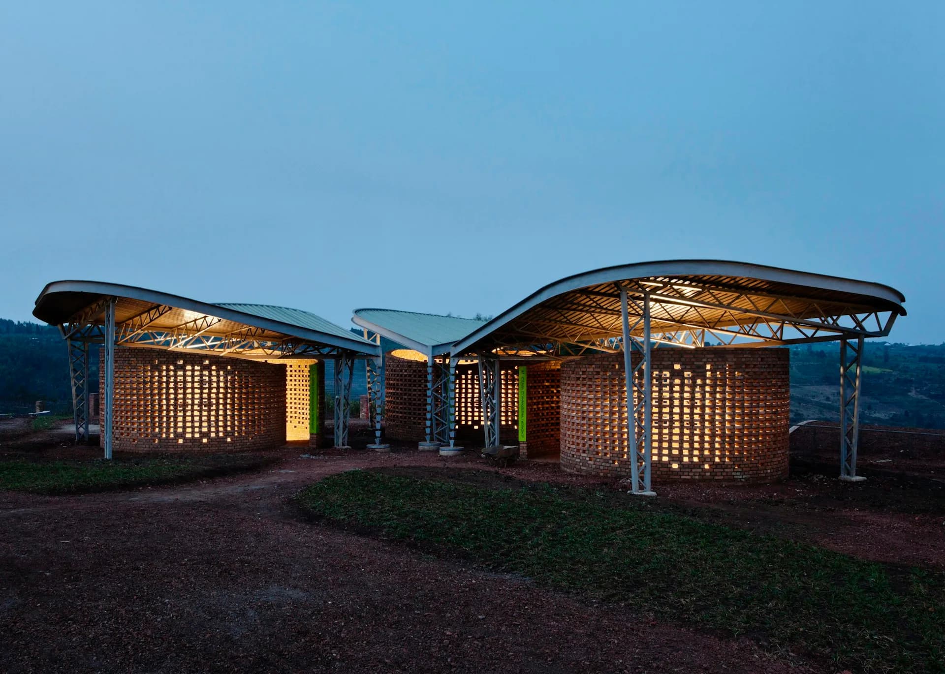 Twilight view of a modern brick pavilion with illuminated latticed walls and curved canopy structures set in a landscape by Sharon Davis Design.