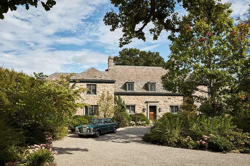 Stone residential exterior with manicured landscaping, gravel driveway, and vintage car, designed by Sheila Bridges Design.