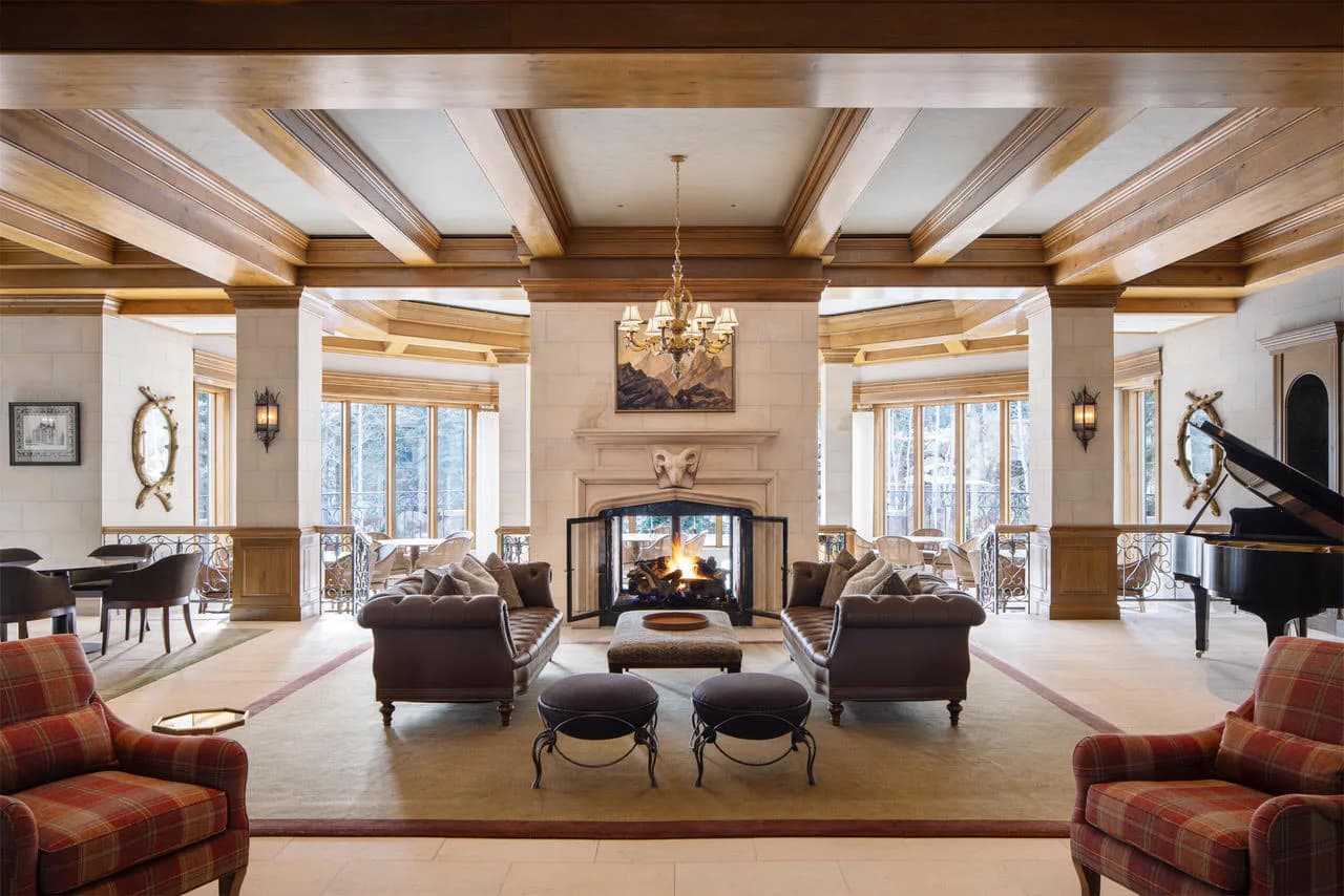 Luxurious living room with coffered ceiling, grand piano, dual fireplaces, and symmetrical seating arrangement in warm wood tones and neutral palette by SheltonMindel℠.