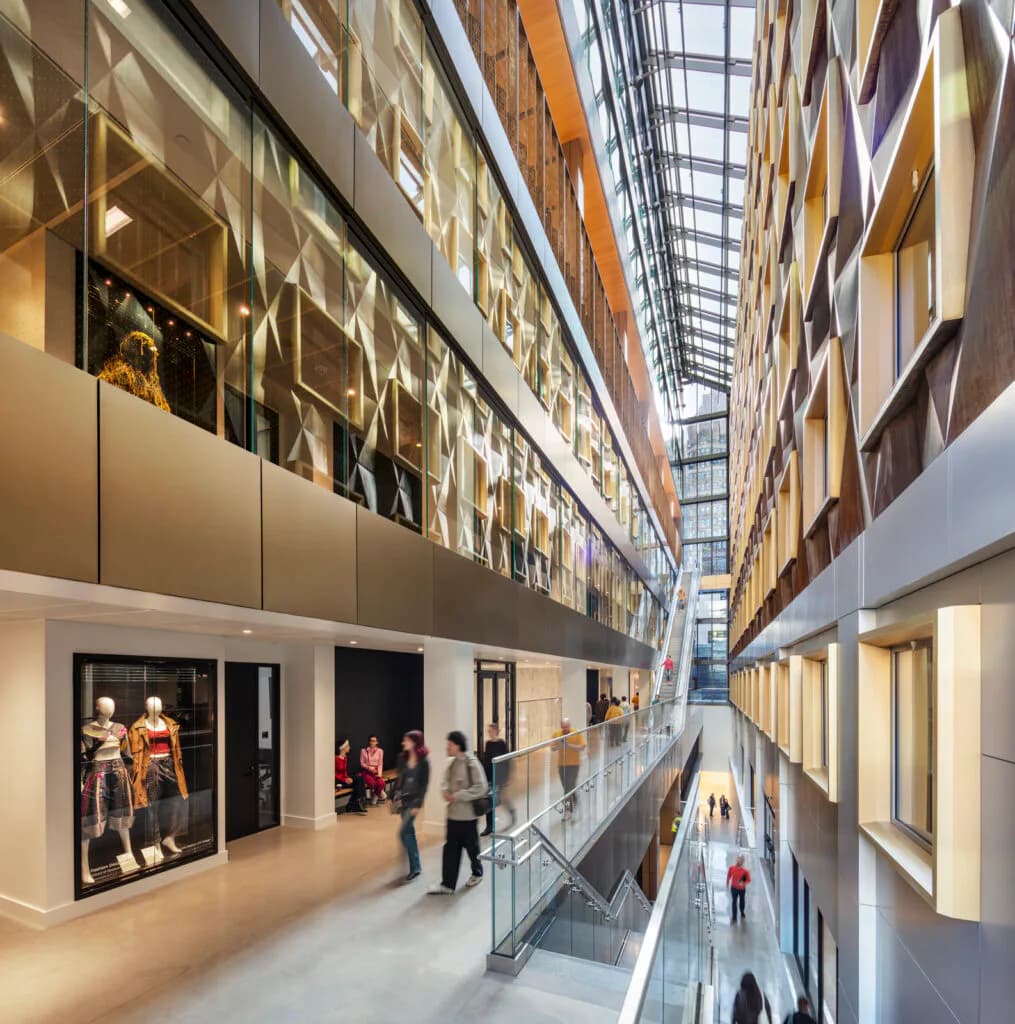 Modern museum atrium with multi-story glazed galleries overlooking a bright central corridor with skylight, featuring warm wood and white finishes by SHoP Architects.