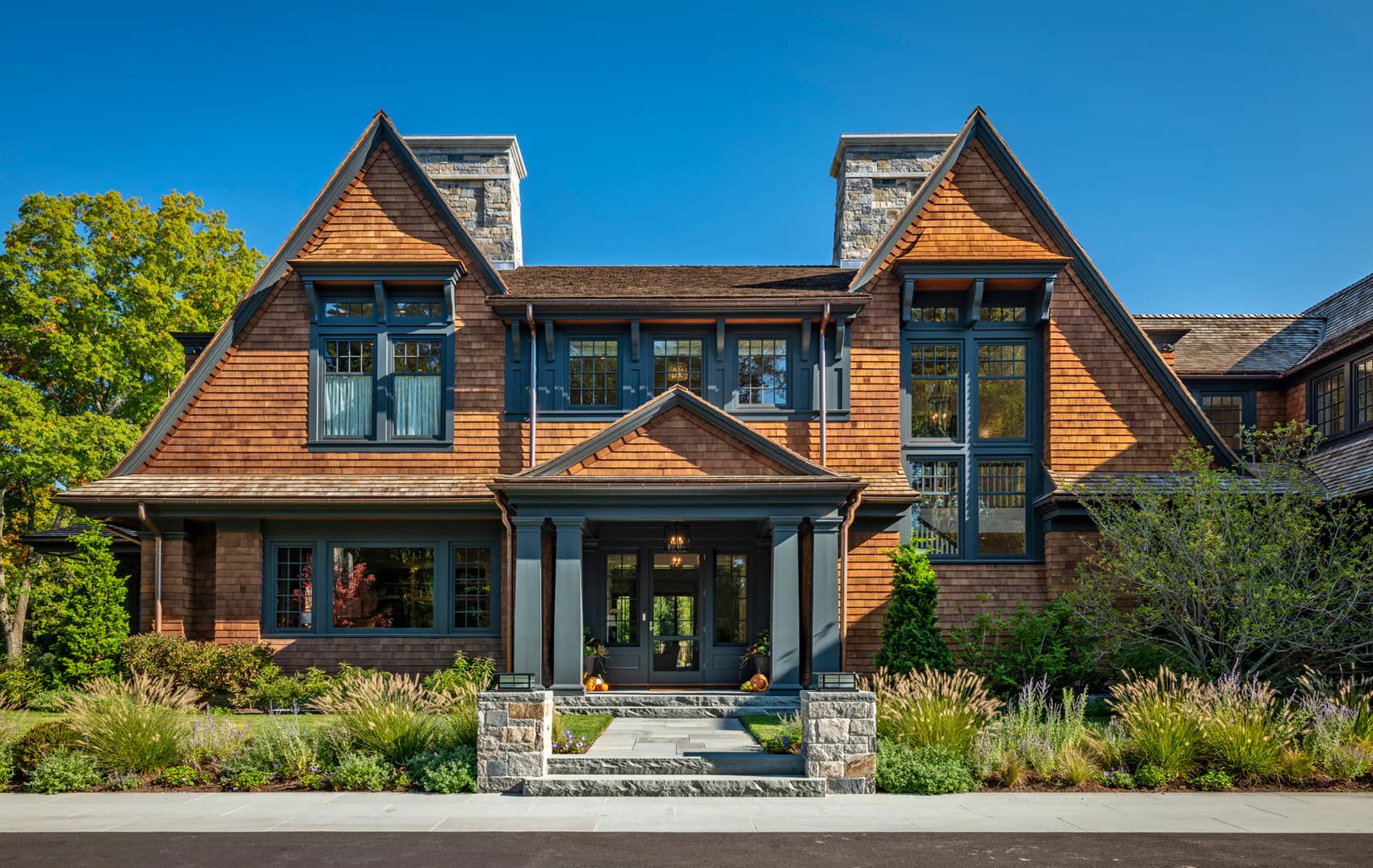 Contemporary residential exterior featuring mixed wood and stone materials, dual gabled rooflines, and extensive glazing overlooking manicured landscaping by Shope Reno Wharton Associates.