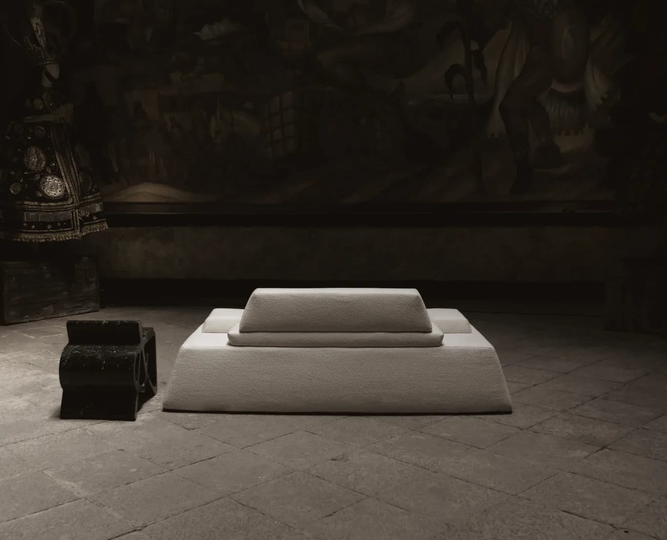 Minimalist interior installation featuring tiered white rectangular platforms on a stone floor, with dark atmospheric lighting and architectural elements visible in background, by Siete Studio.