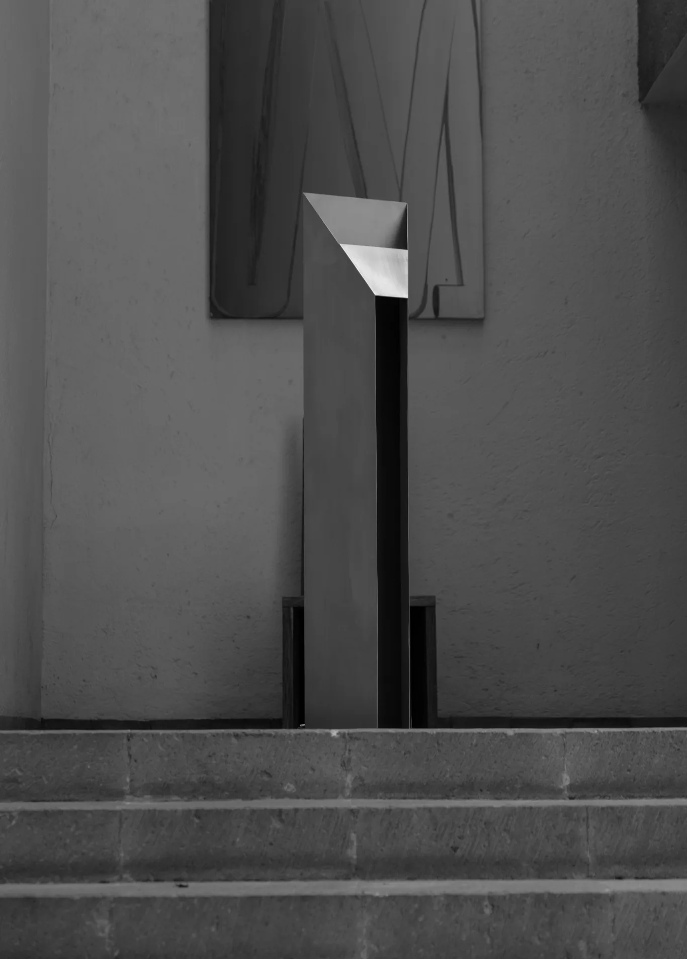 Minimalist architectural installation featuring a black vertical column with white geometric element at top, flanked by draped gray fabric panels, by Siete Studio.