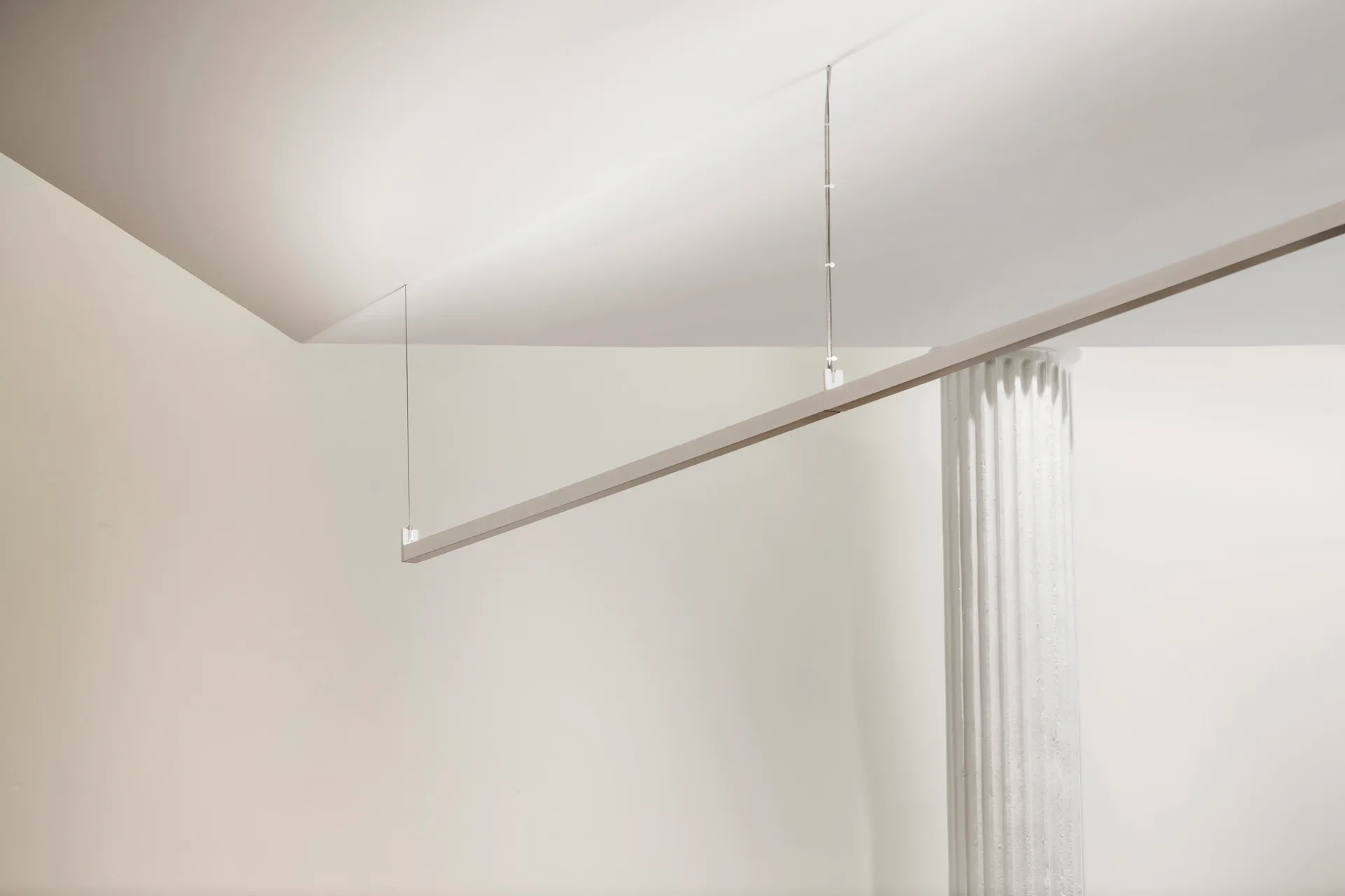Minimalist interior with suspended linear pendant light fixture and vertical blinds against white walls and ceiling by Sighte Studio.