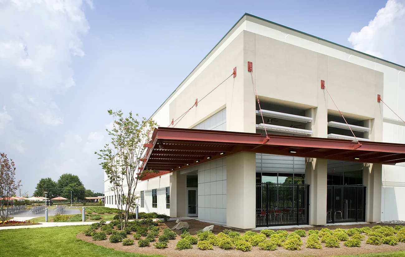 Modern white building with red metal accents and large windows, surrounded by landscaping and green lawn, designed by Sigma7 design group.