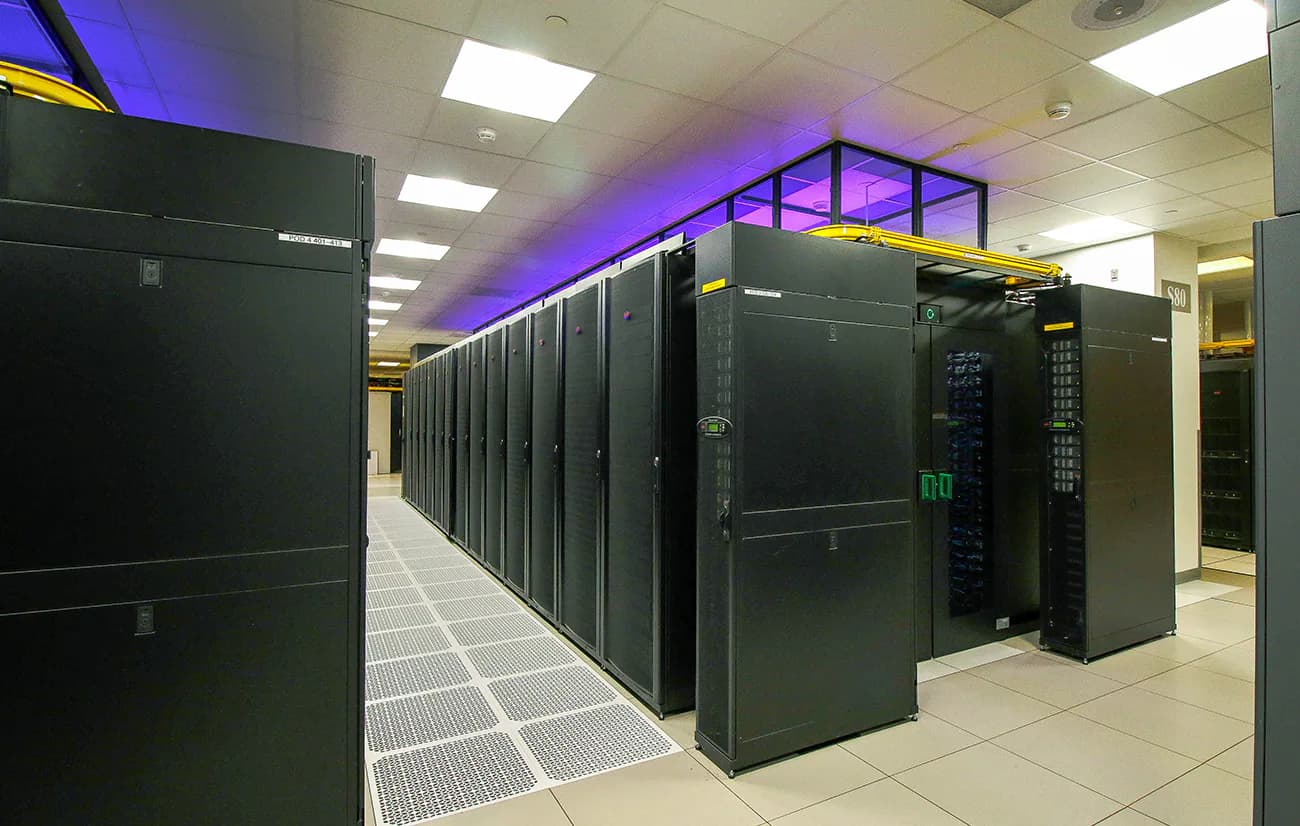 Modern data center corridor with black server cabinets arranged in rows, featuring purple accent lighting and polished concrete flooring, designed by Sigma7 design group.