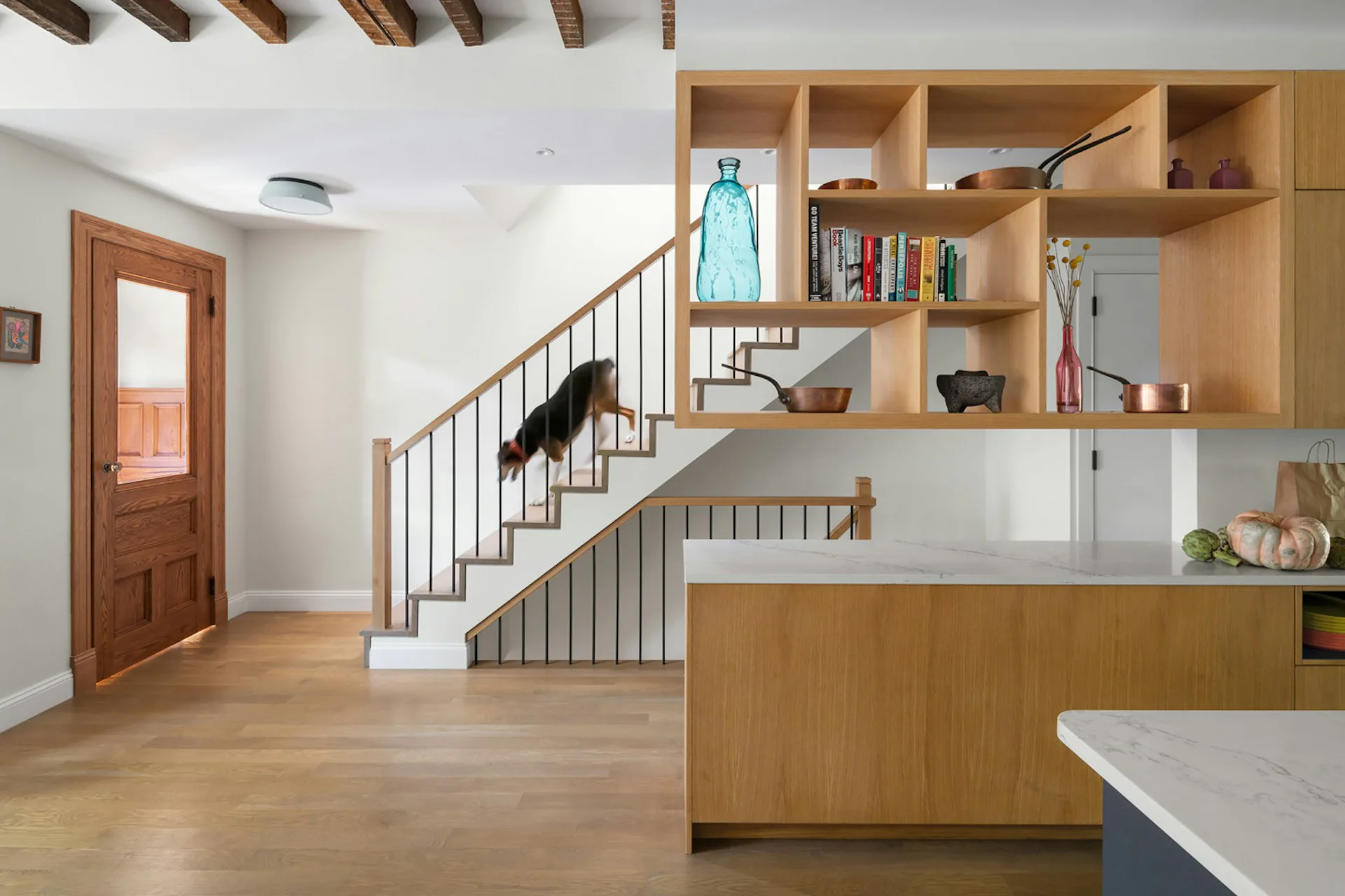 Modern residential interior with natural wood cabinetry, built-in shelving, staircase with metal railings, and light oak flooring by Siris Coombs Architecture.