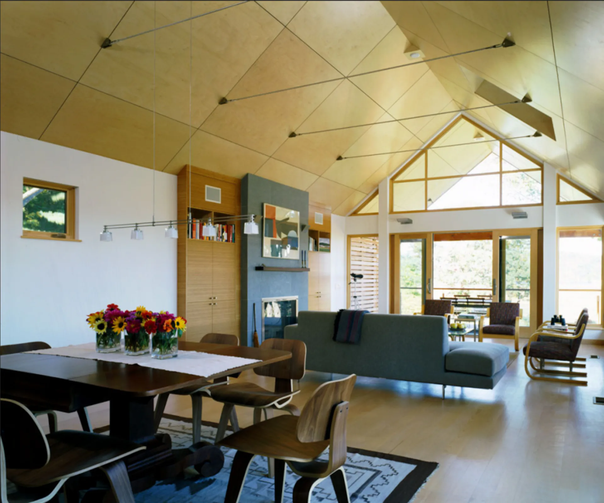 Modern open-plan living space with vaulted wooden ceiling, green sofa, dining area, and expansive glazing, by Siris Coombs Architecture.