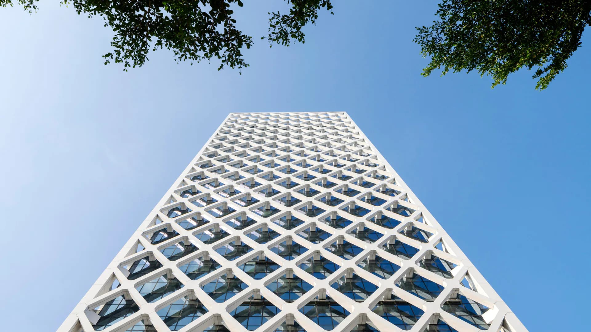 Soaring white lattice tower with geometric diamond pattern photographed from below against clear blue sky, designed by Skidmore, Owings & Merrill.