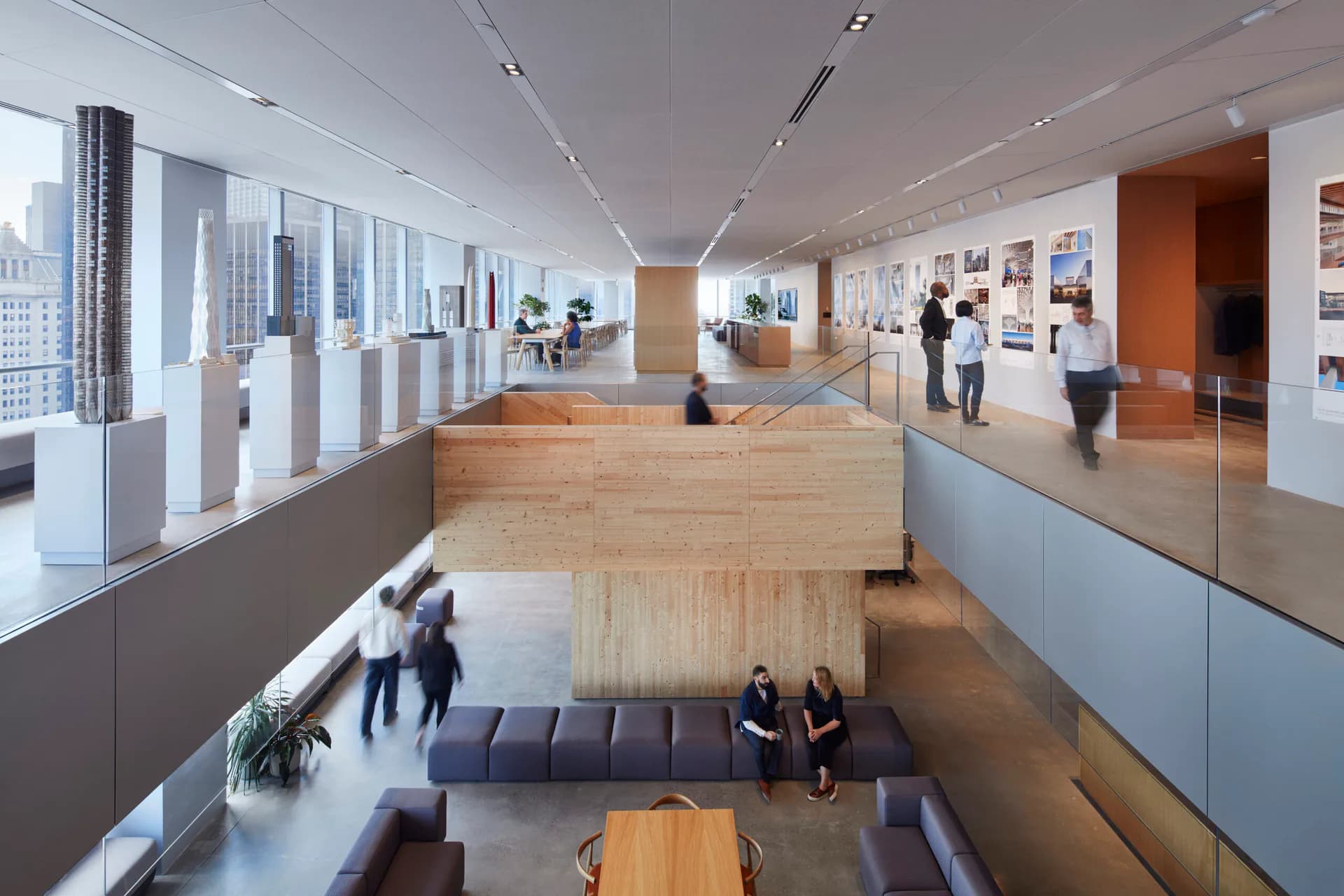 Modern multi-level interior gallery space with light wood platform, white walls, floor-to-ceiling windows, and synthetic figures, designed by Skidmore, Owings & Merrill.