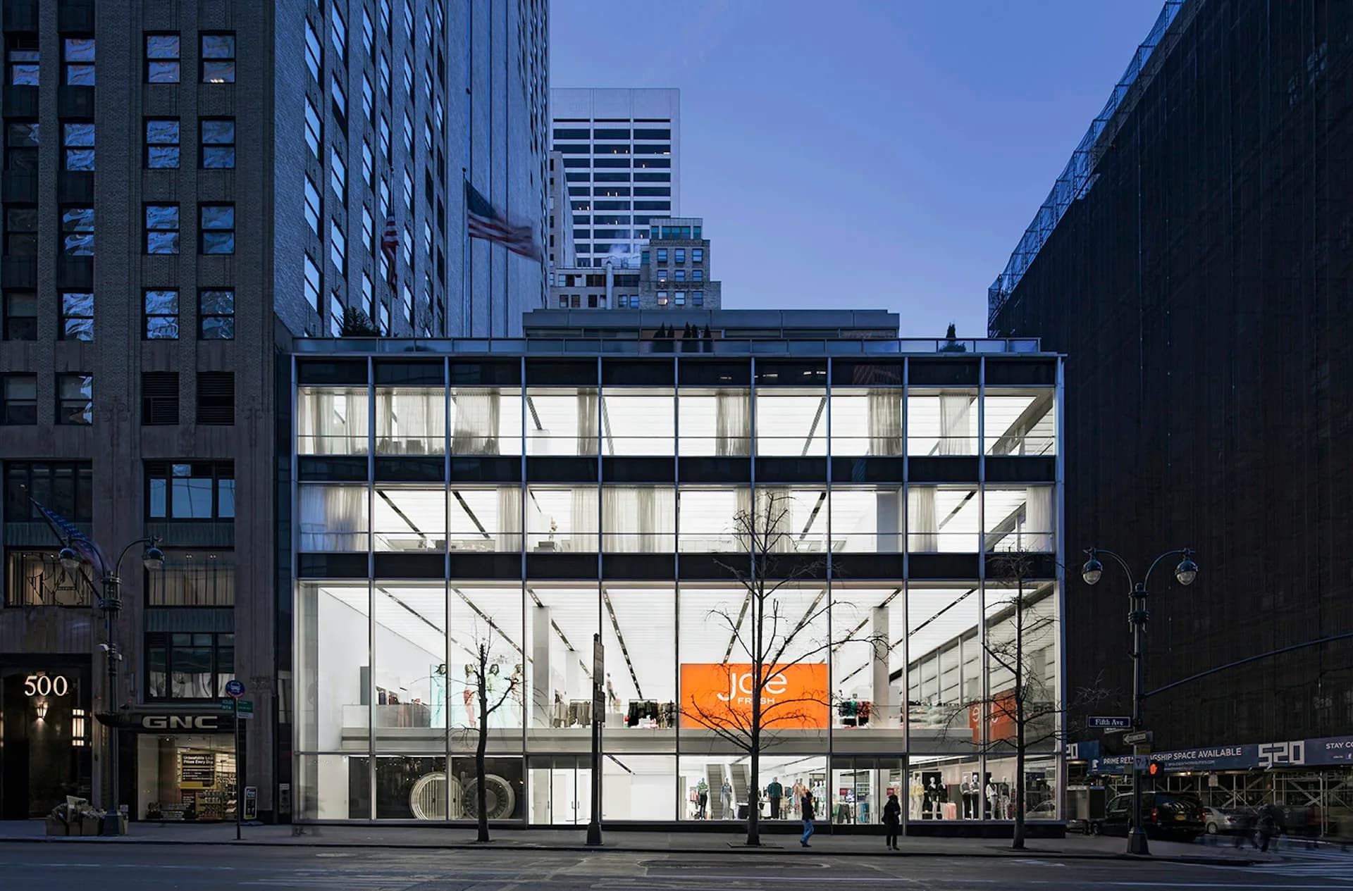 Modern glass-fronted building with steel framework and orange interior accent, located on an urban street surrounded by tall office buildings, photographed by Skidmore, Owings & Merrill (SOM).