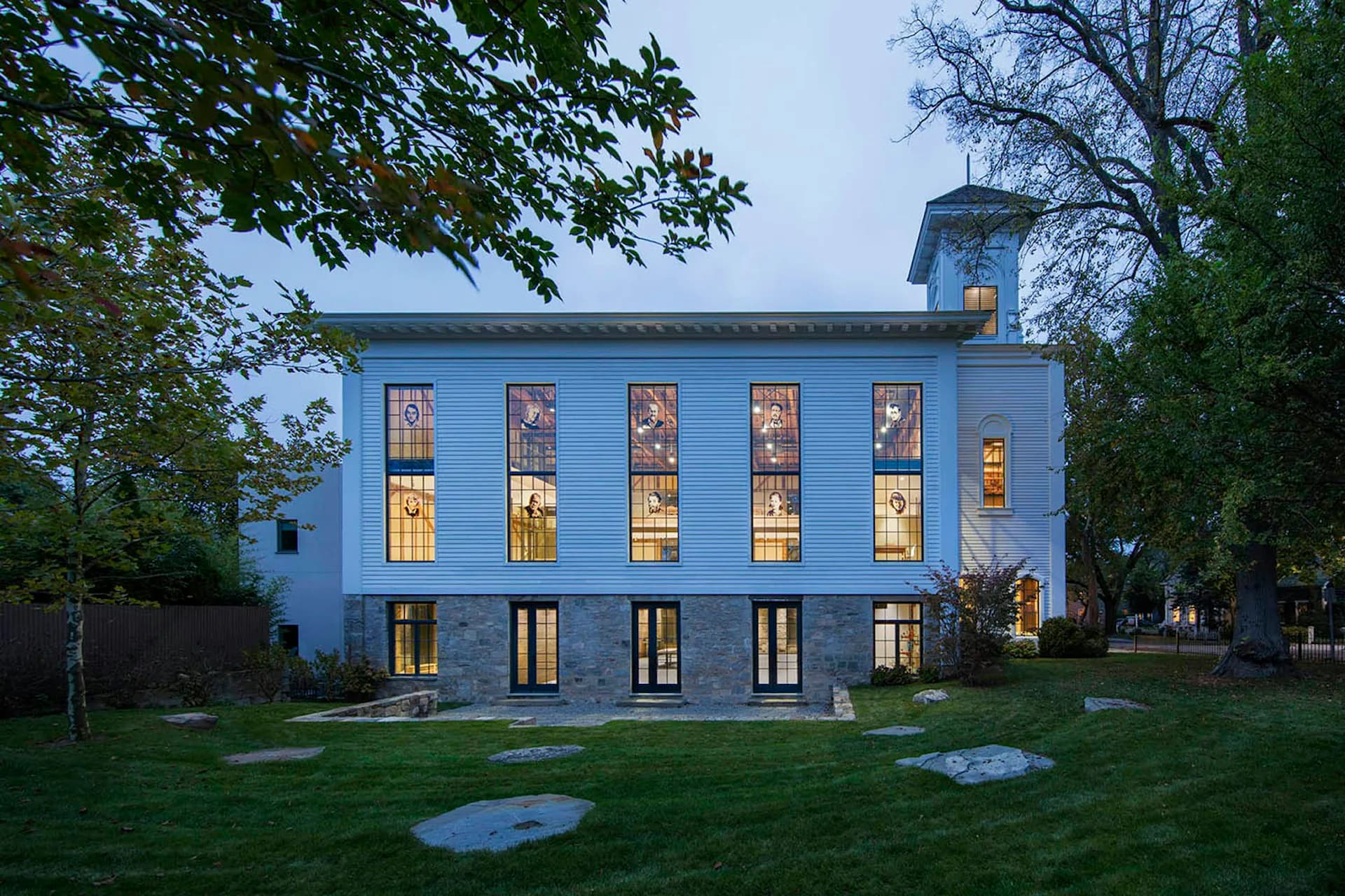 Twilight exterior of a striking blue residential building with illuminated windows, manicured lawn, and modern architectural details by SKOLNICK Architecture.