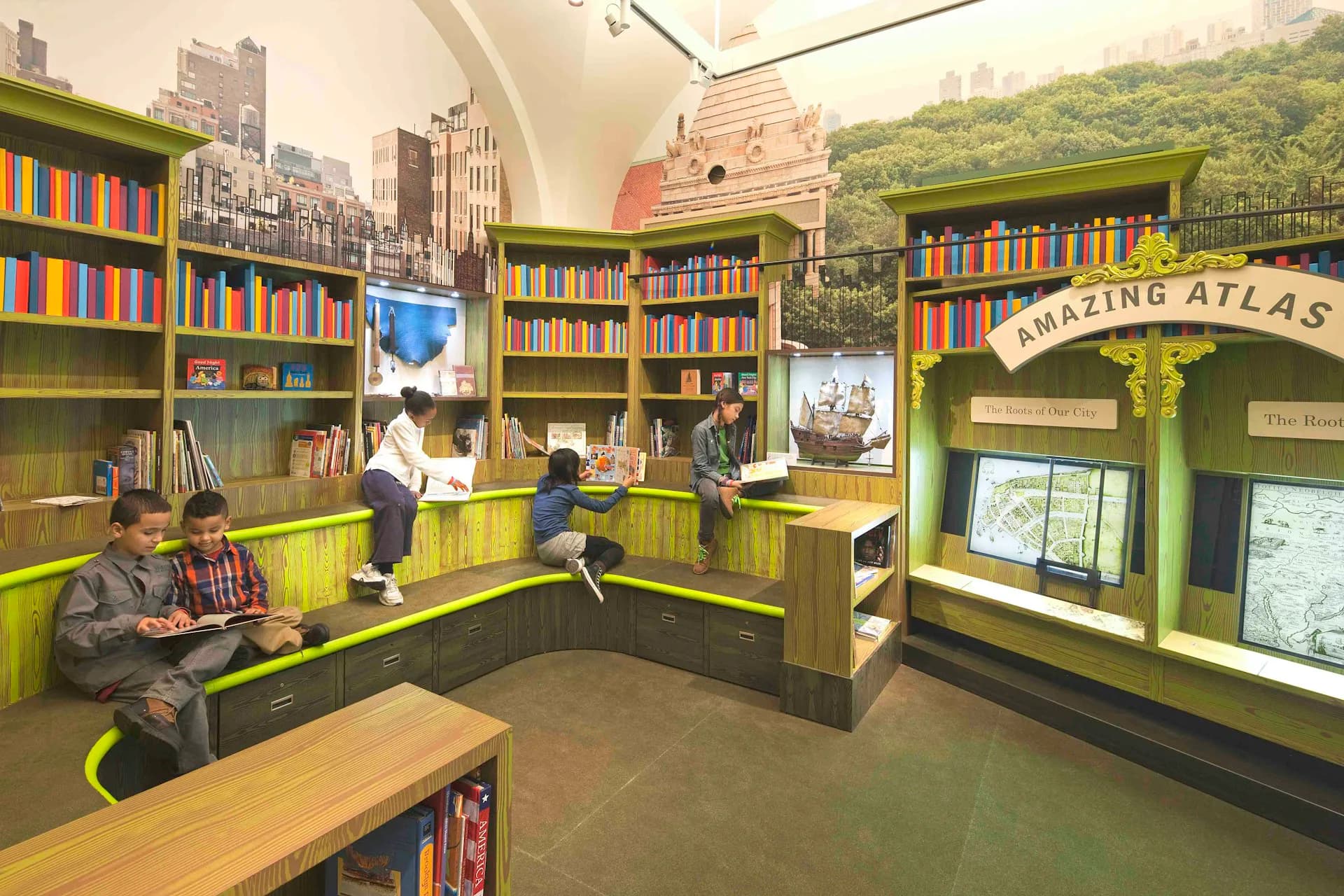 Bright green library interior with colorful bookshelves, natural wood tables, and mural depicting city skyline, designed by SKOLNICK Architecture.
