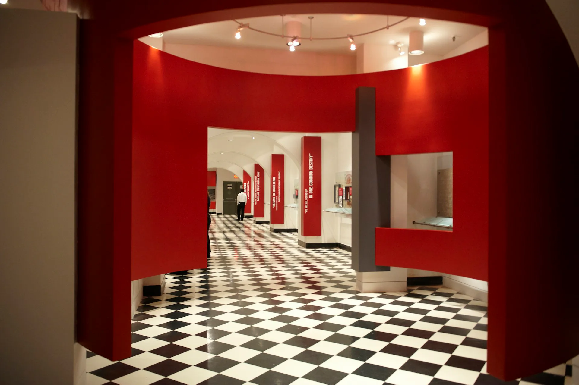 Red-walled gallery space with black-and-white checkered flooring and curved architectural elements by SKOLNICK Architecture.