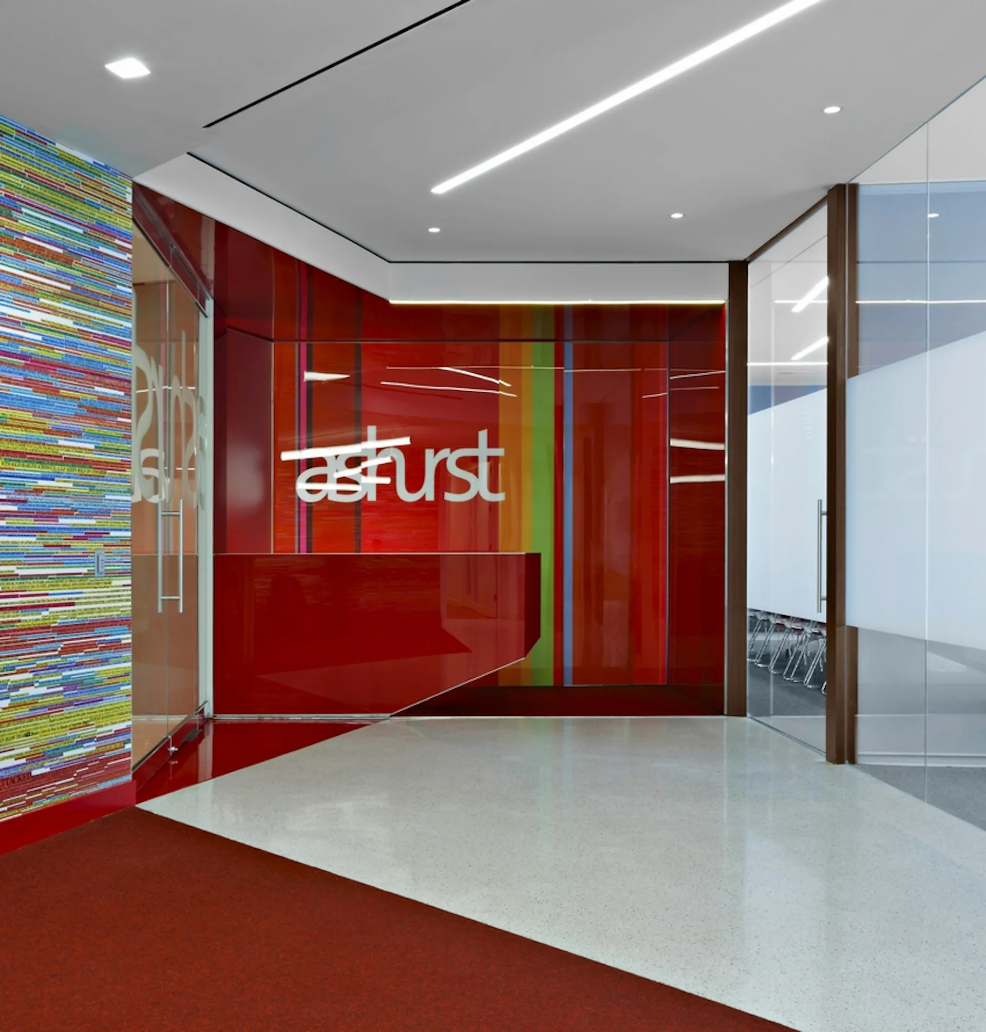 Modern office reception area featuring vibrant red glazed walls with green accent panels, colorful pixelated feature wall, linear ceiling lights, and polished concrete flooring by SLADE ARCHITECTURE.