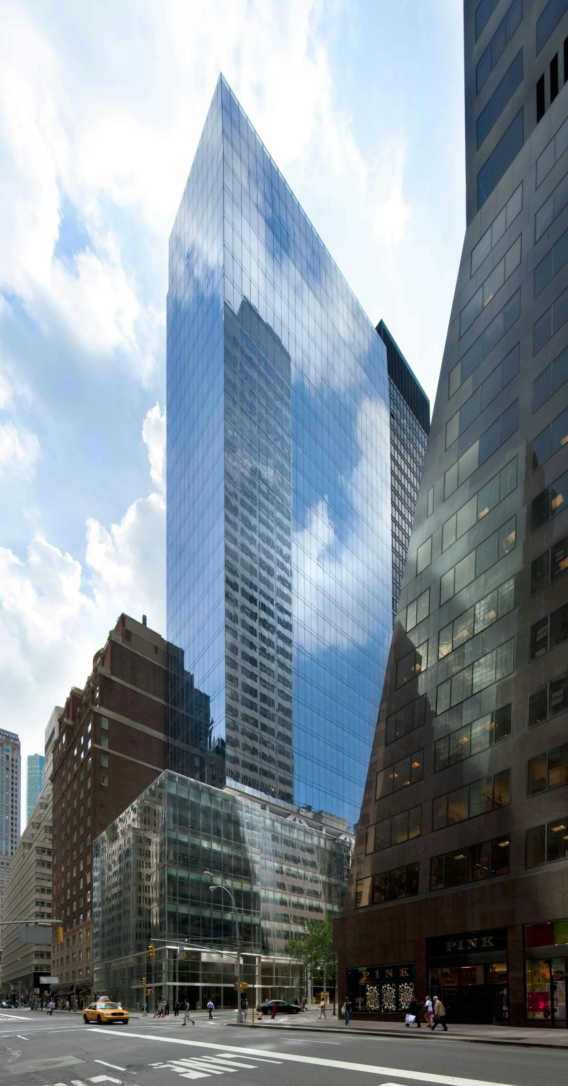 Modern glass-clad skyscraper with reflective blue facade towering above surrounding brick buildings on a Manhattan street by SLCE Architects, LLP.