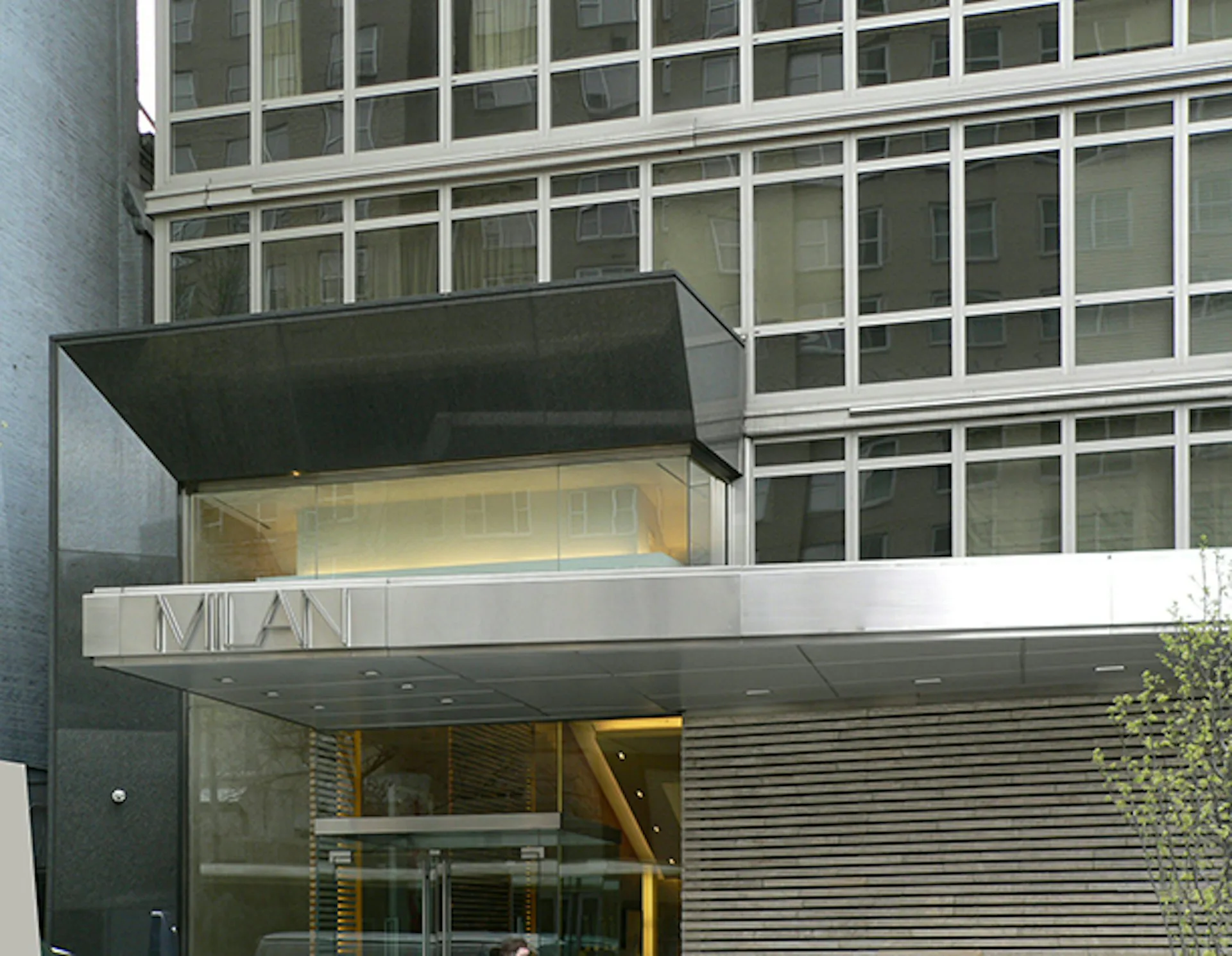 Modern storefront with dark canopy, glass facade, and metal shutter, featuring minimalist design and yellow interior accents by SLCE Architects, LLP.