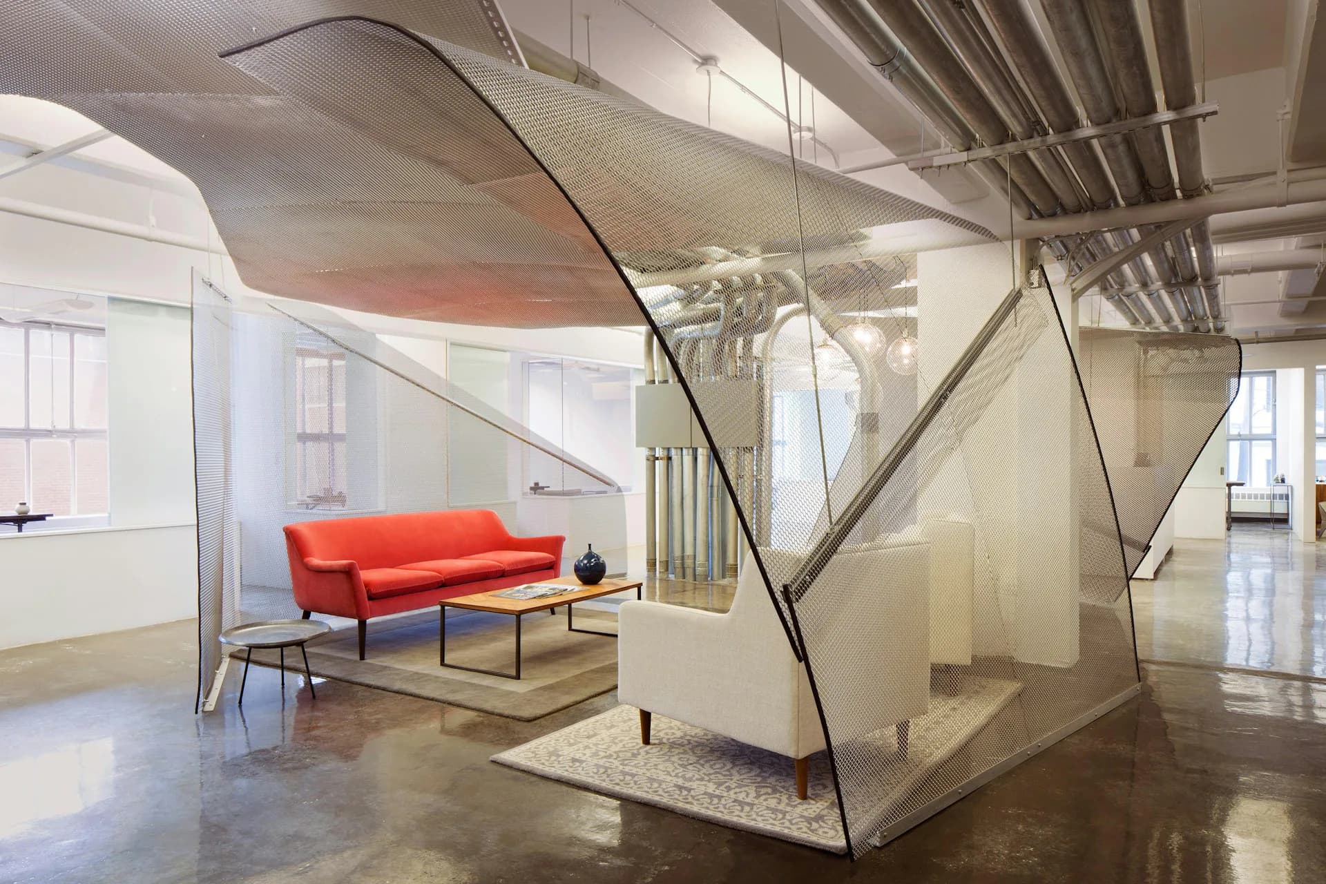 Modern loft interior featuring a striking geometric glass partition, orange mid-century sofa, polished concrete floors, and industrial ceiling details by Smith and Architects.