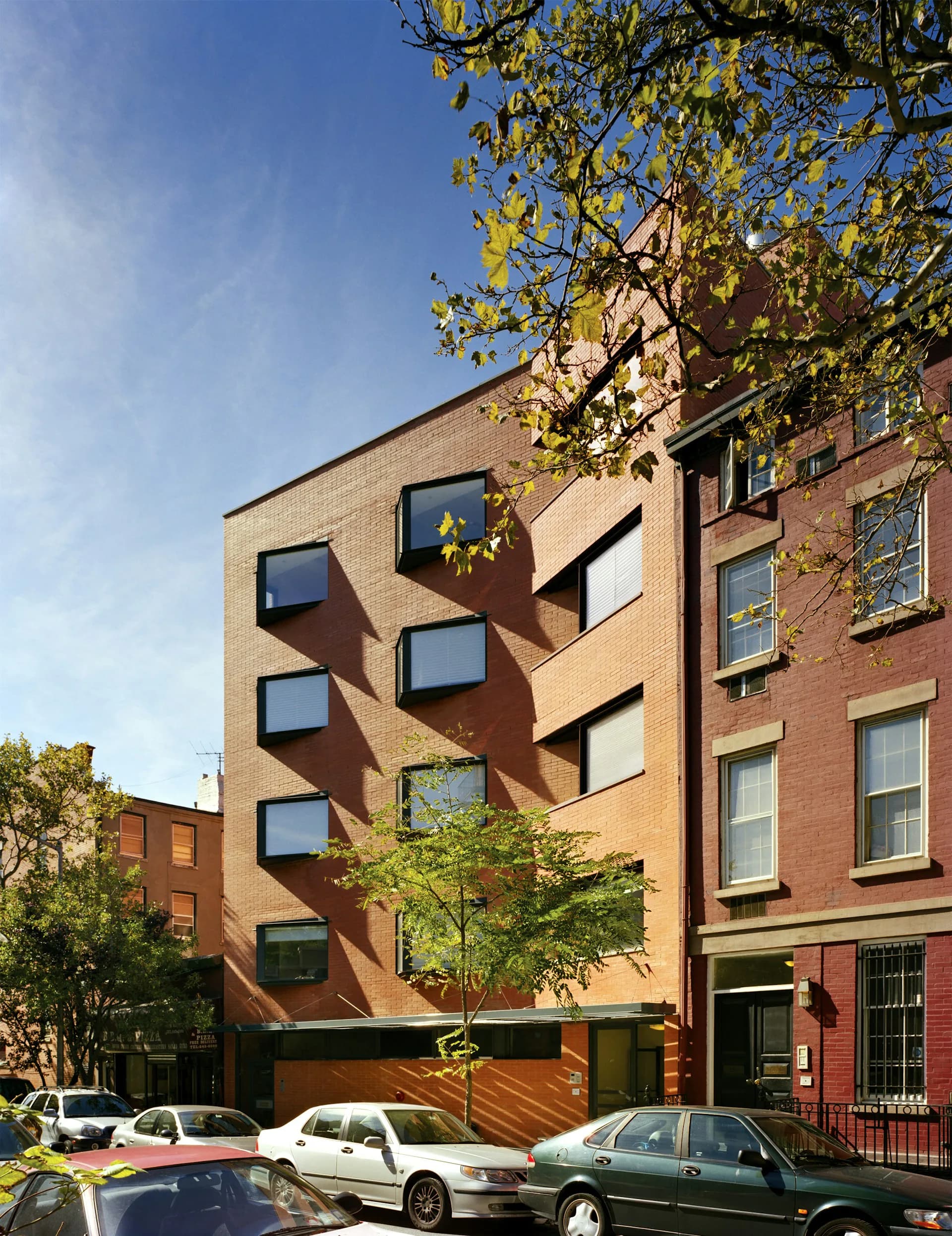 Brick residential building with geometric window pattern and warm terracotta façade designed by Smith-Miller + Hawkinson Architects LLP, street-level view with parked cars.