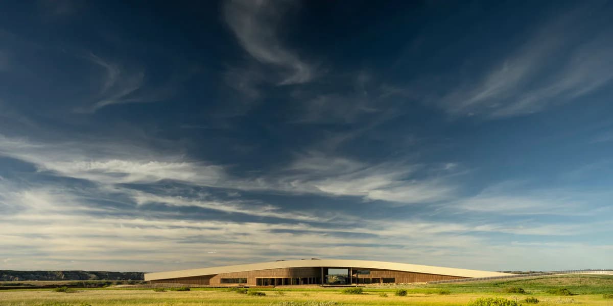 Expansive prairie landscape with modernist low-profile building structure set against dramatic cloudy sky, designed by Snøhetta New York.