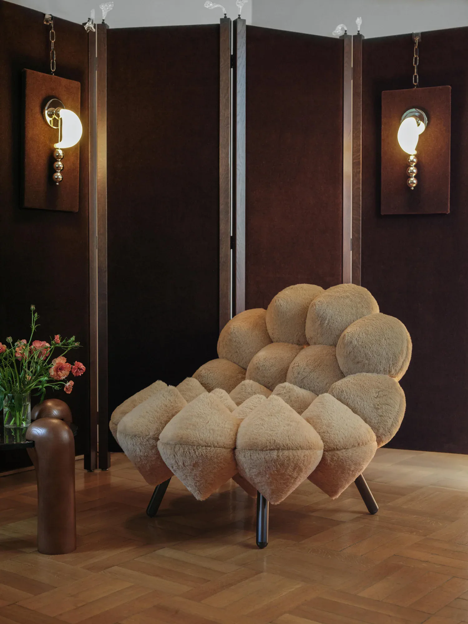 Sculptural cloud-shaped upholstered chair in cream fabric displayed in a gallery setting with dark wood paneling, decorative lighting, and fresh flowers by Soft Witness.