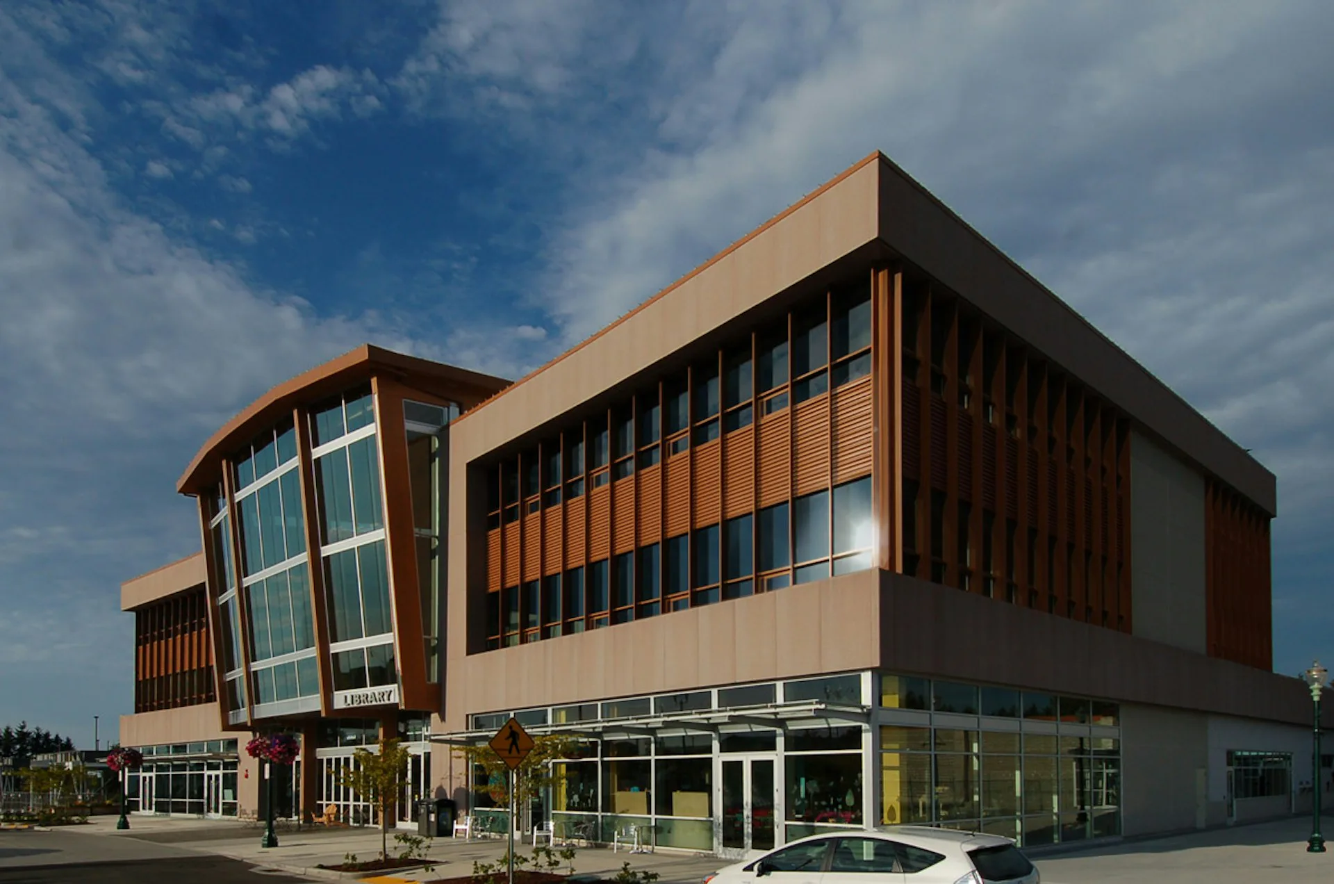 Modern institutional building with curved glass facade, orange and dark wood cladding, and ground-level glazing under blue sky by Soluri Architecture.
