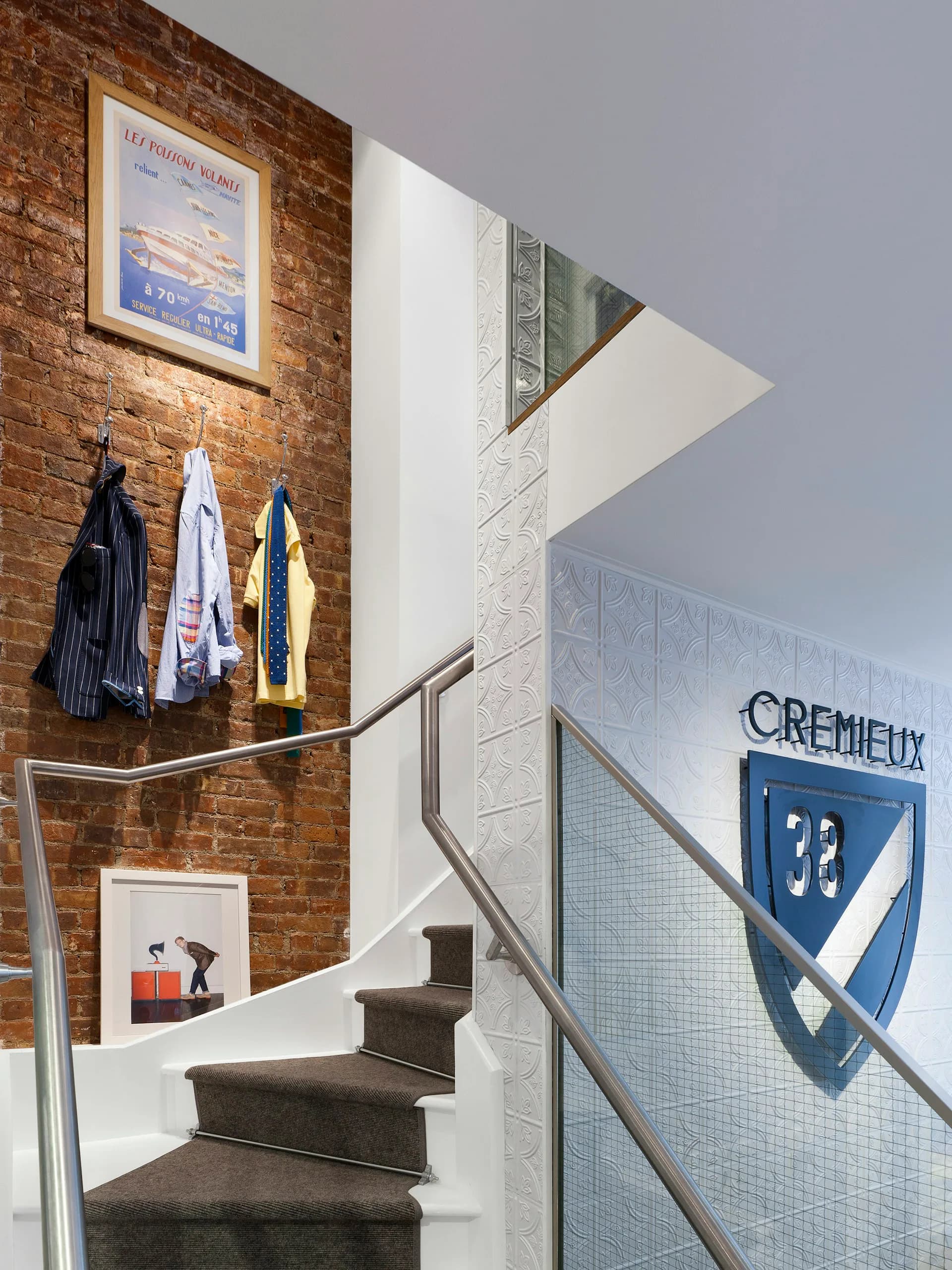 Modern stairwell with exposed brick wall, floating stairs, metal railings, and blue Cremieux signage by Spacesmith.