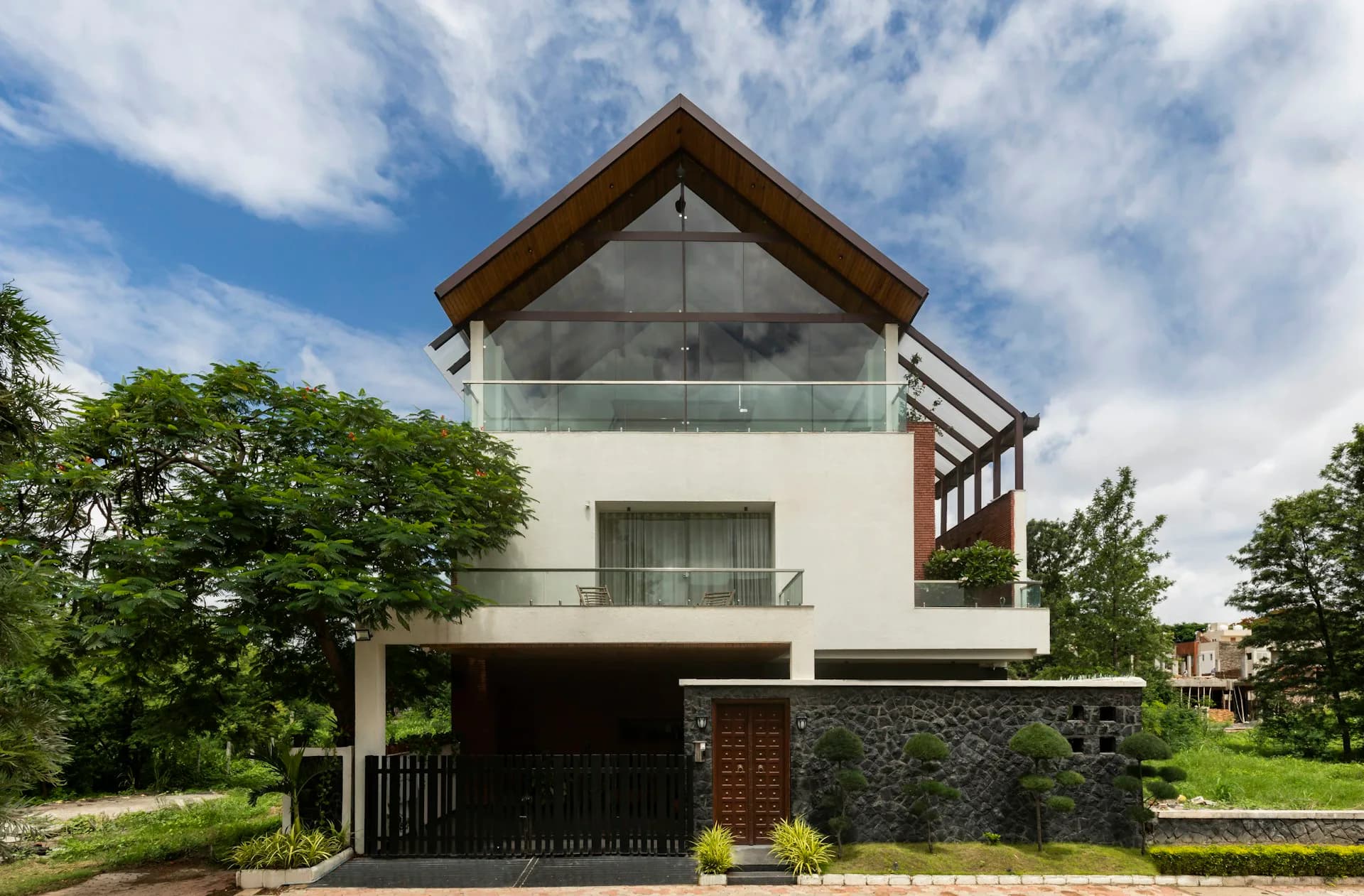 Modern residential building with white walls, wooden roof overhang, and dark stone base, surrounded by green landscaping by SPAN ARCHITECTS.