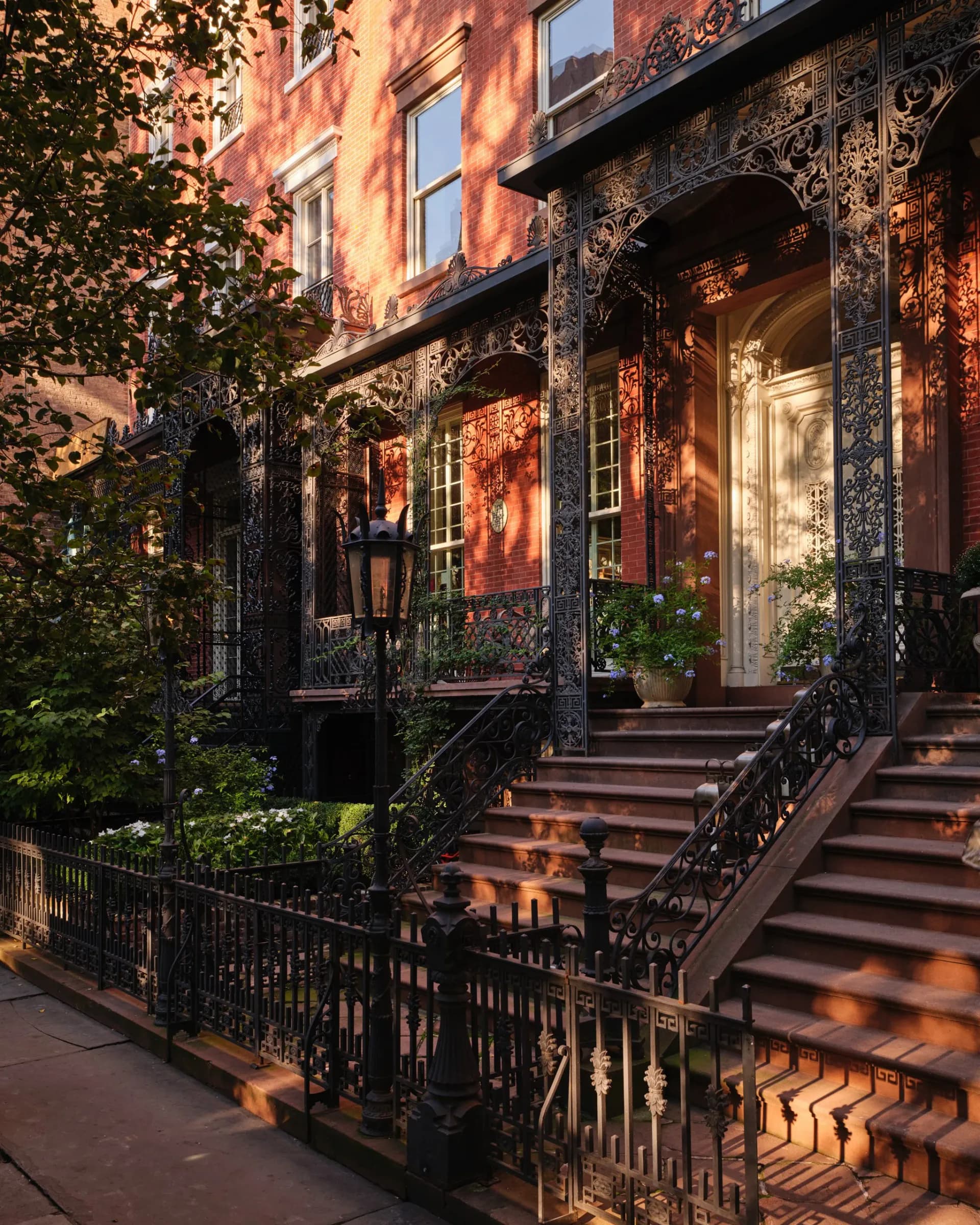 Warm-toned brownstone facade with ornate black ironwork, ivy-covered entrance, and golden sunset lighting by SPAN ARCHITECTS.