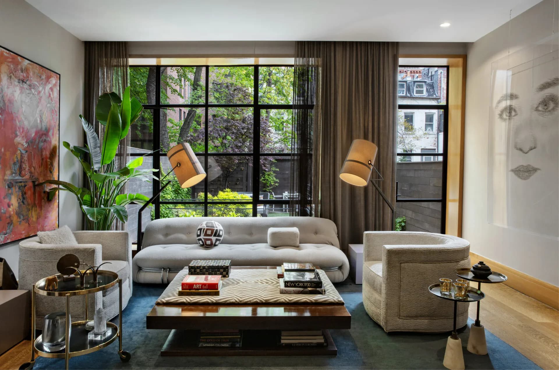 Contemporary living room with curved gray sofa, wooden coffee table, blue area rug, large black-framed windows, potted plants, and modern artwork by SPAN ARCHITECTS.