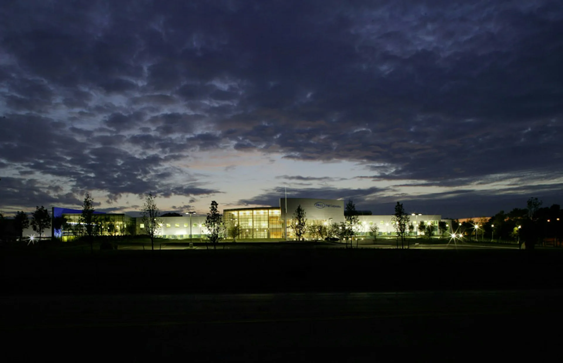 Illuminated modern institutional building with glass facades reflected against dramatic twilight sky, surrounded by landscaping, by Spectorgroup.