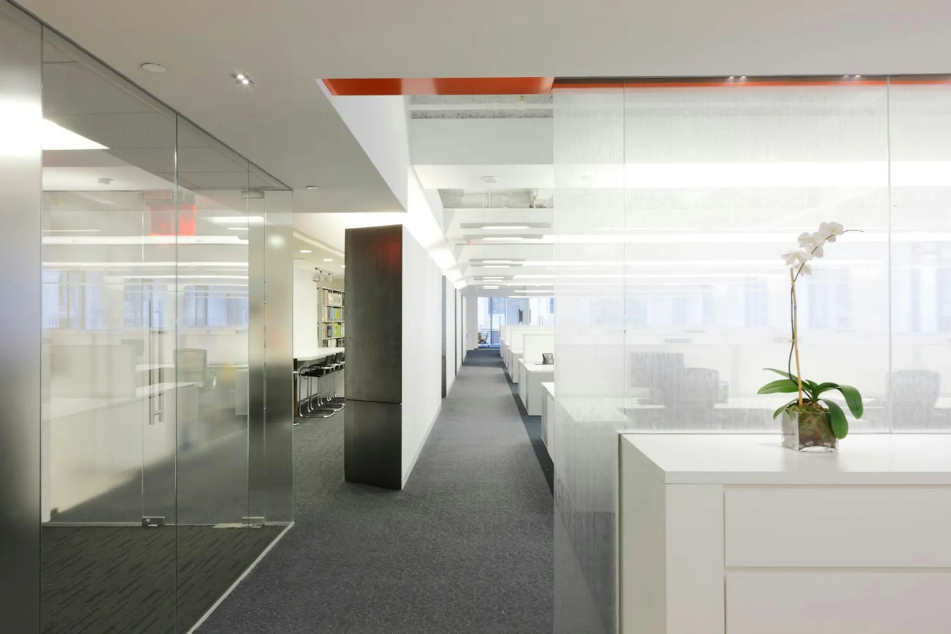 Modern office interior with white cabinetry, glass partitions, grey flooring, and minimalist furnishings by Spectorgroup.