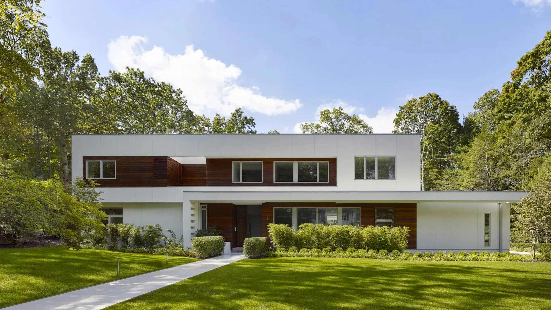 Modern two-story residential home with white and dark brown facades, expansive lawn, and mature trees, designed by SPG Architects.