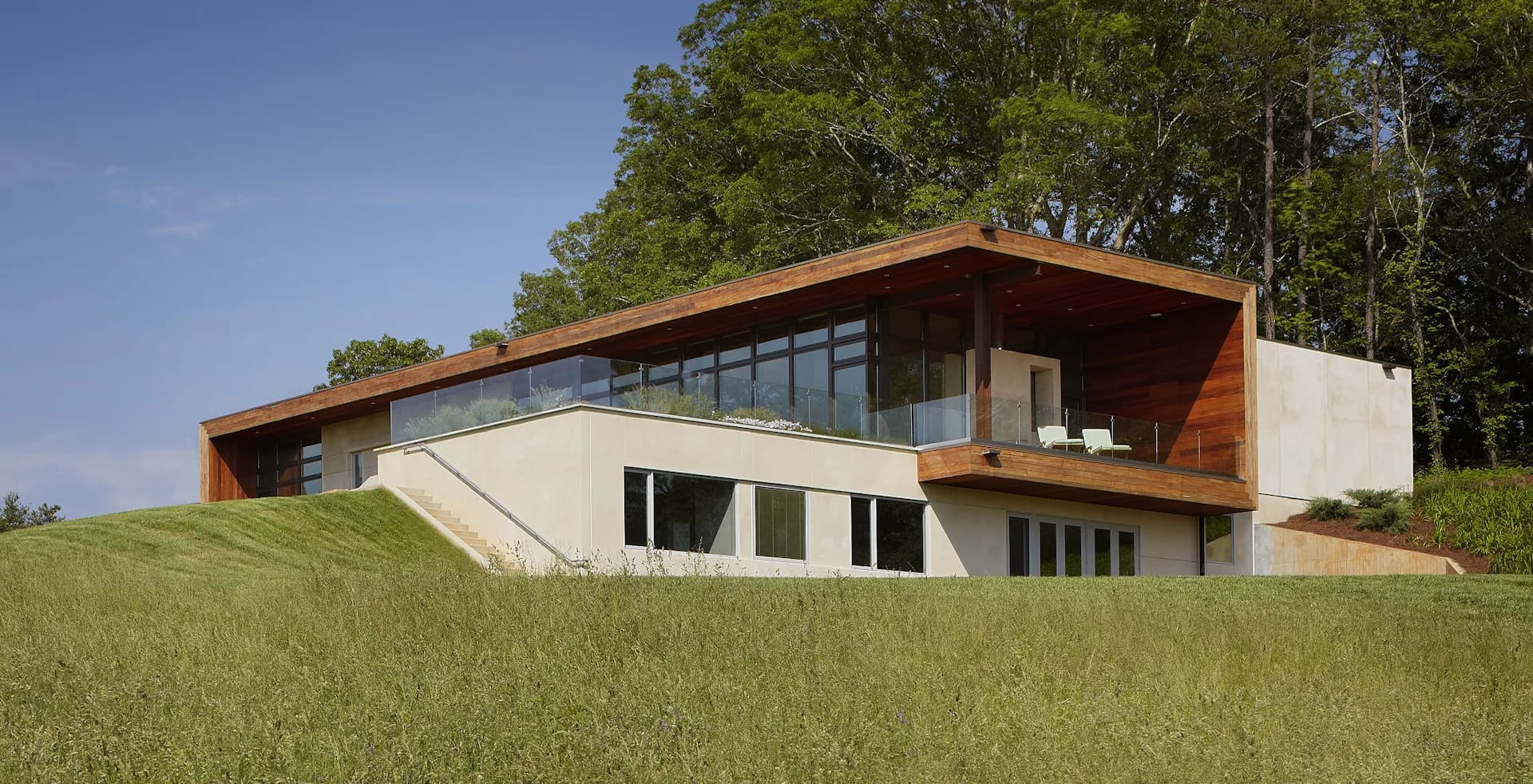 Modern residential building with curved copper roofline and white concrete lower level nestled into sloping green landscape by SPG Architects.