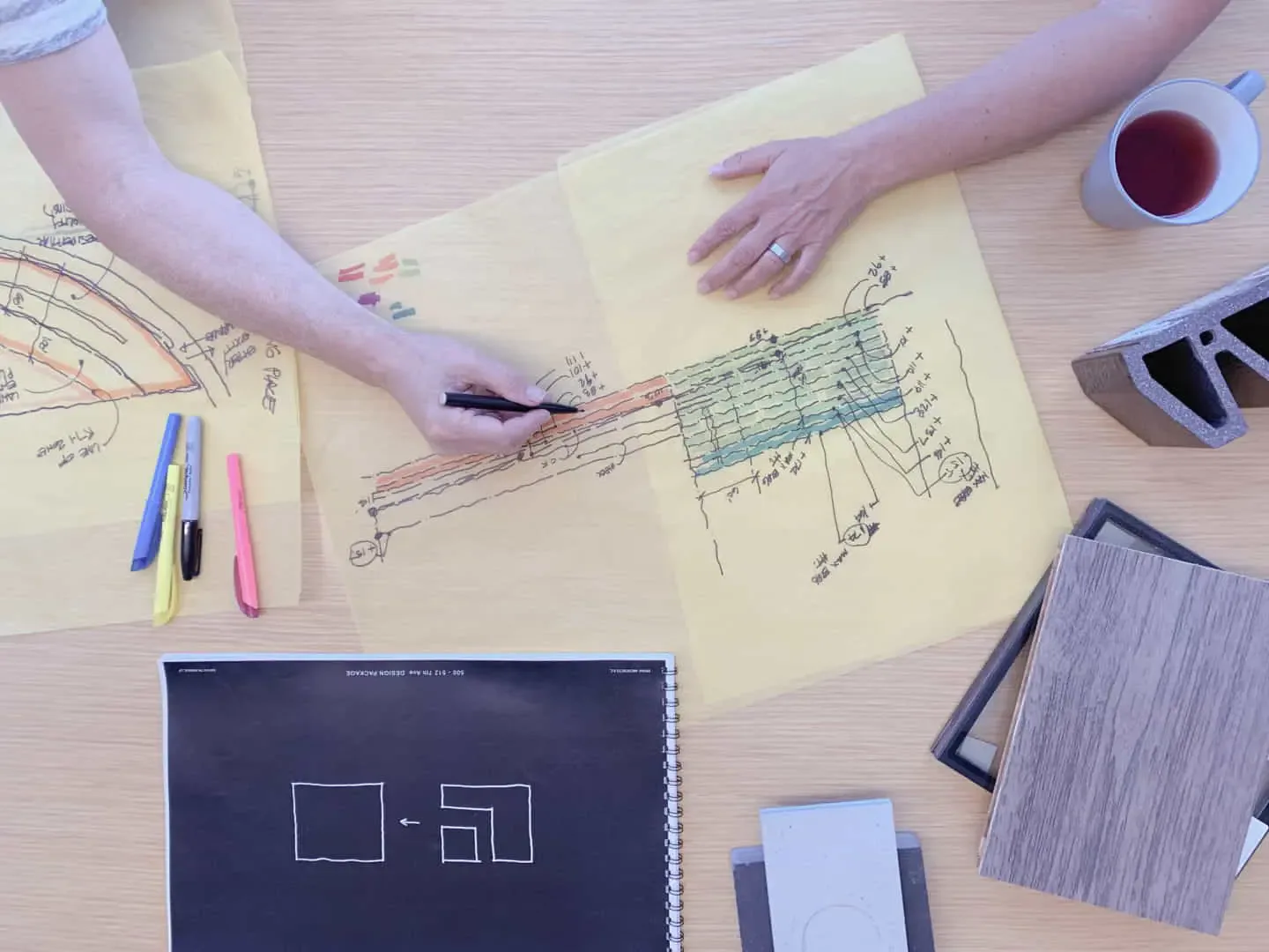 Designer's workspace with architectural sketches, material samples, and colored pencils on a wooden desk by Spivak Architects.