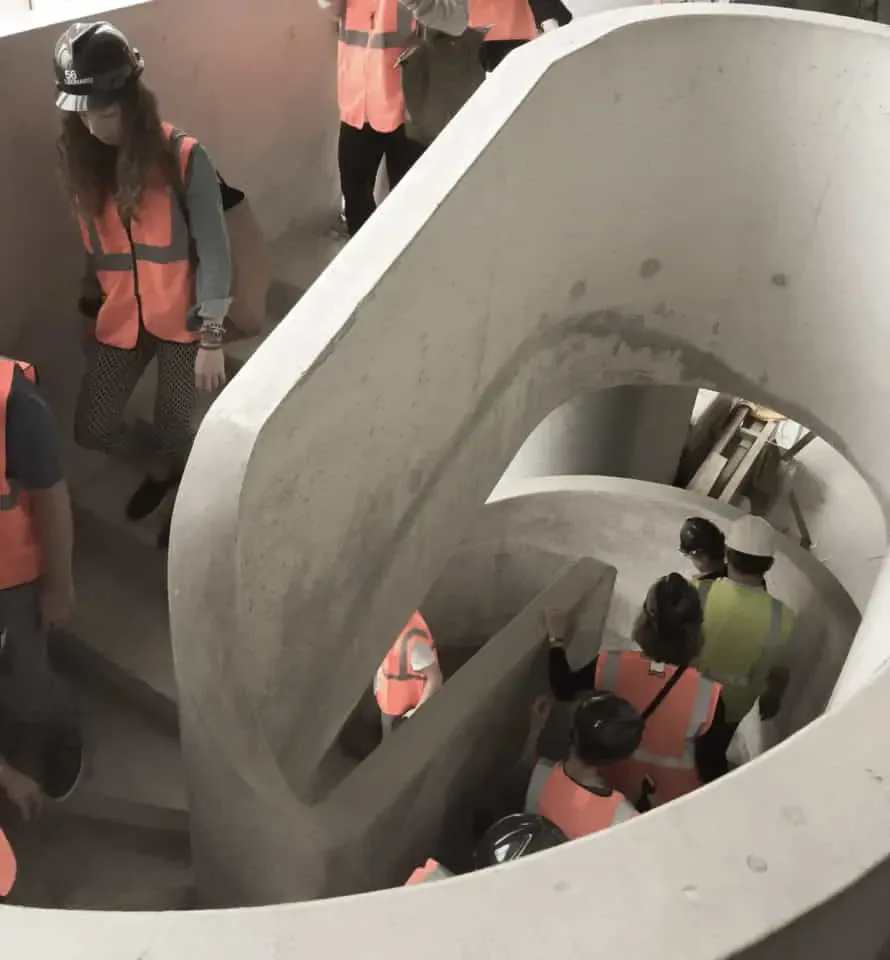 Concrete spiral staircase with curved geometric forms and people in safety vests descending, designed by Spivak Architects.