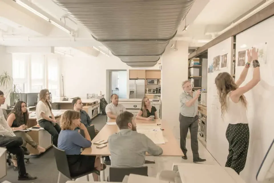 Bright open-plan office space with natural light, collaborative workspace featuring round tables, exposed ceiling, and whiteboard wall installations by Spivak Architects.