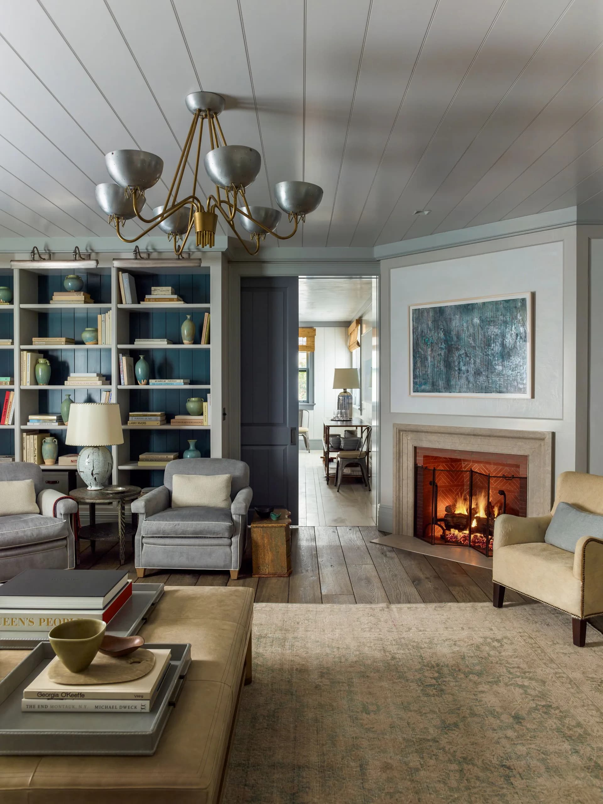 Elegant living room with blue-painted built-in bookshelves, brass chandelier, fireplace with artwork above, neutral upholstered seating, and wood coffee table by S.R. Gambrel.