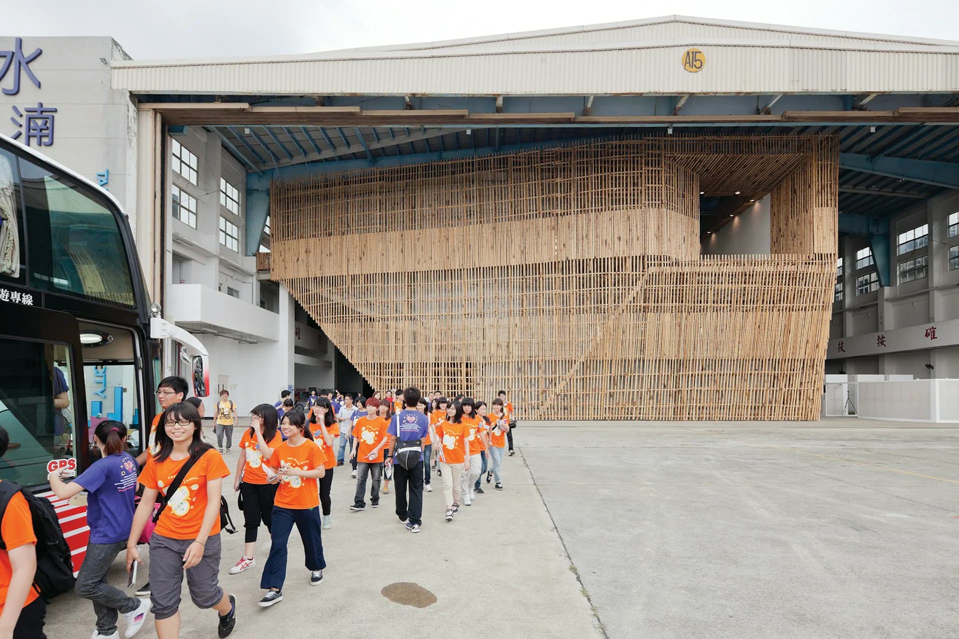 Large industrial warehouse space with woven bamboo screening installation and concrete floor, visited by groups in safety vests, by Stan Allen Architect.