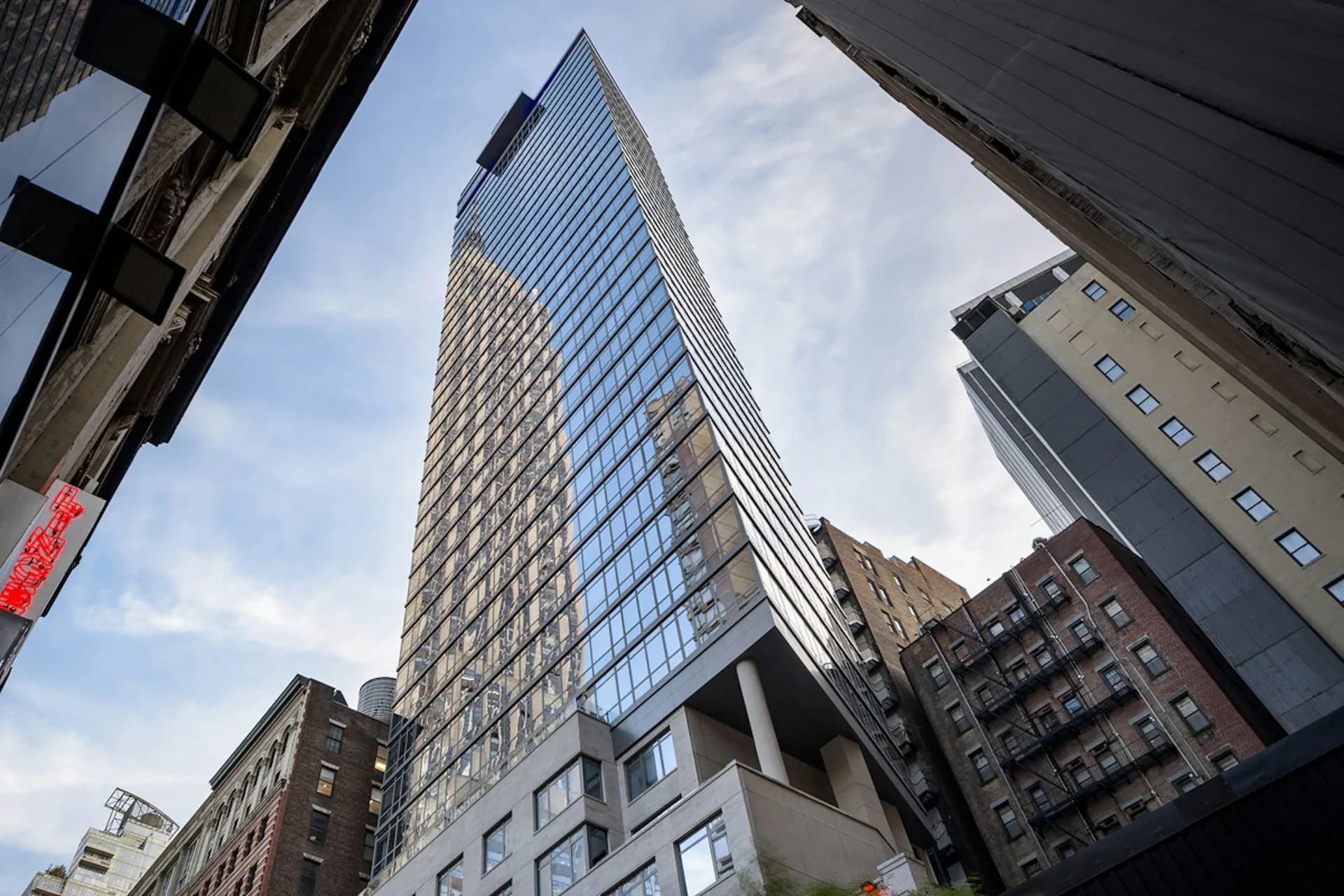Tall modern glass and steel tower with gridded facade rises among historic brick buildings in urban streetscape, designed by SBJ Group.