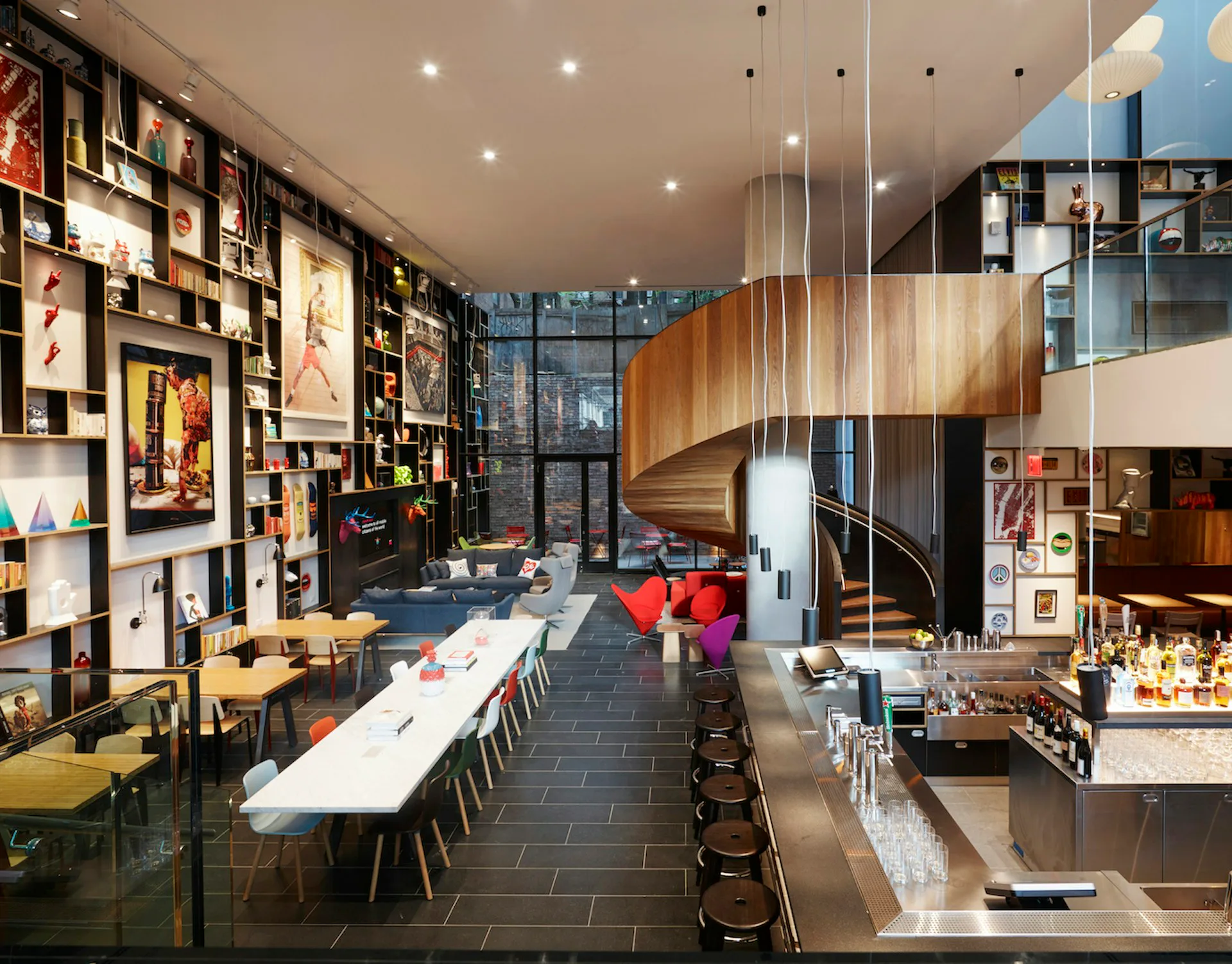 Modern loft interior with spiral staircase, long dining table, dark tile flooring, wooden architectural elements, and floor-to-ceiling shelving by SBJ Group.